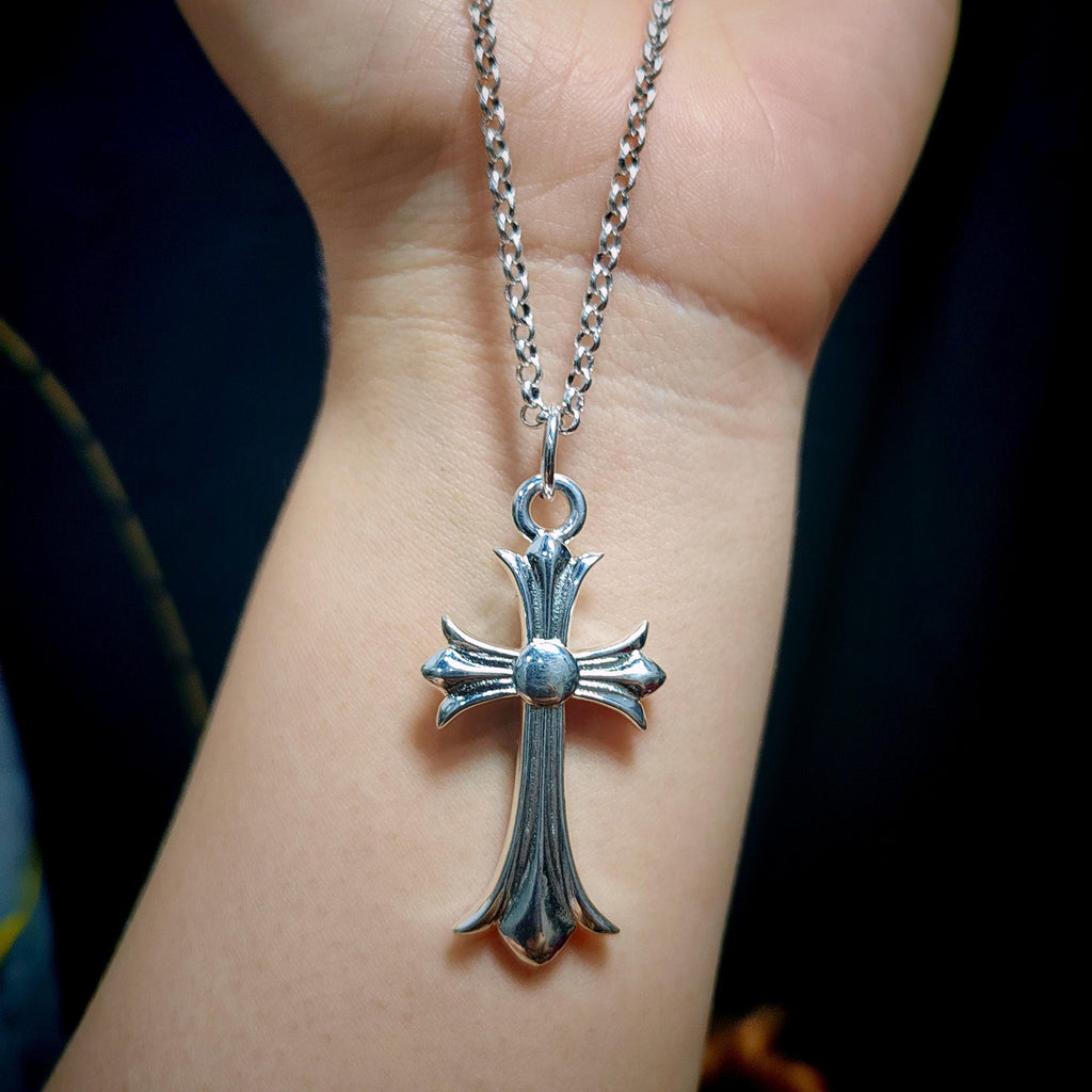 Silver cross pendant necklace on a person's wrist with a dark background