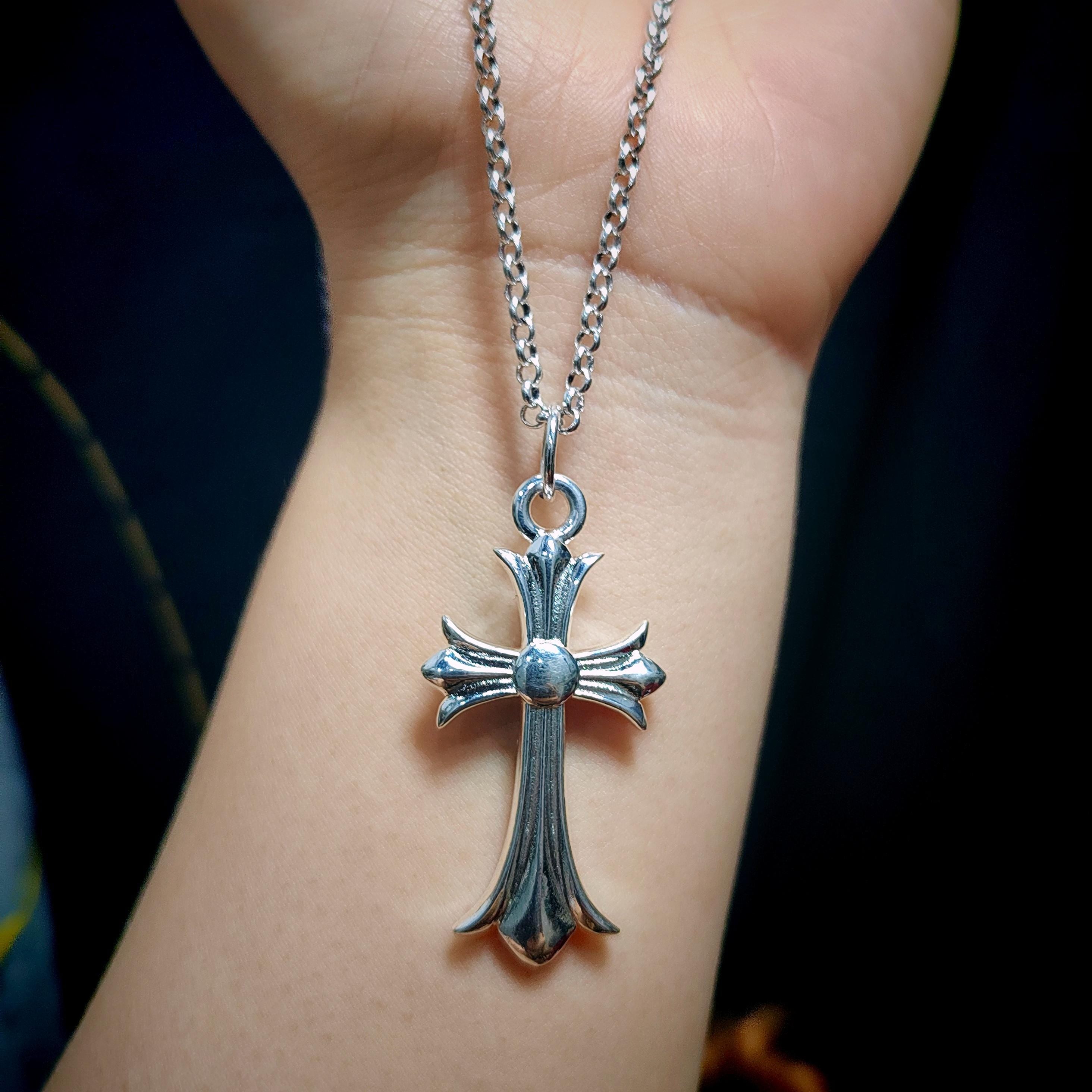 Silver cross pendant necklace on a person's wrist with a dark background