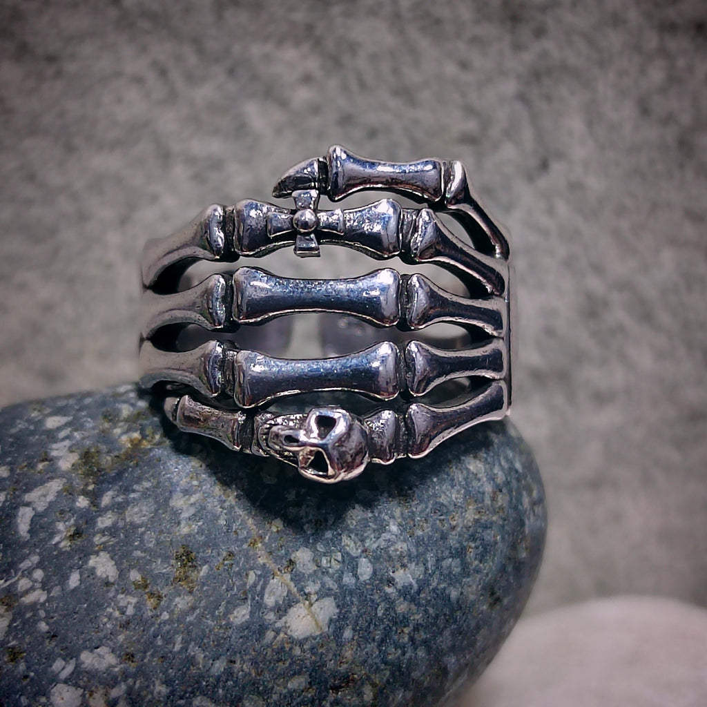 Silver skeleton hand ring on a textured stone surface with a neutral background