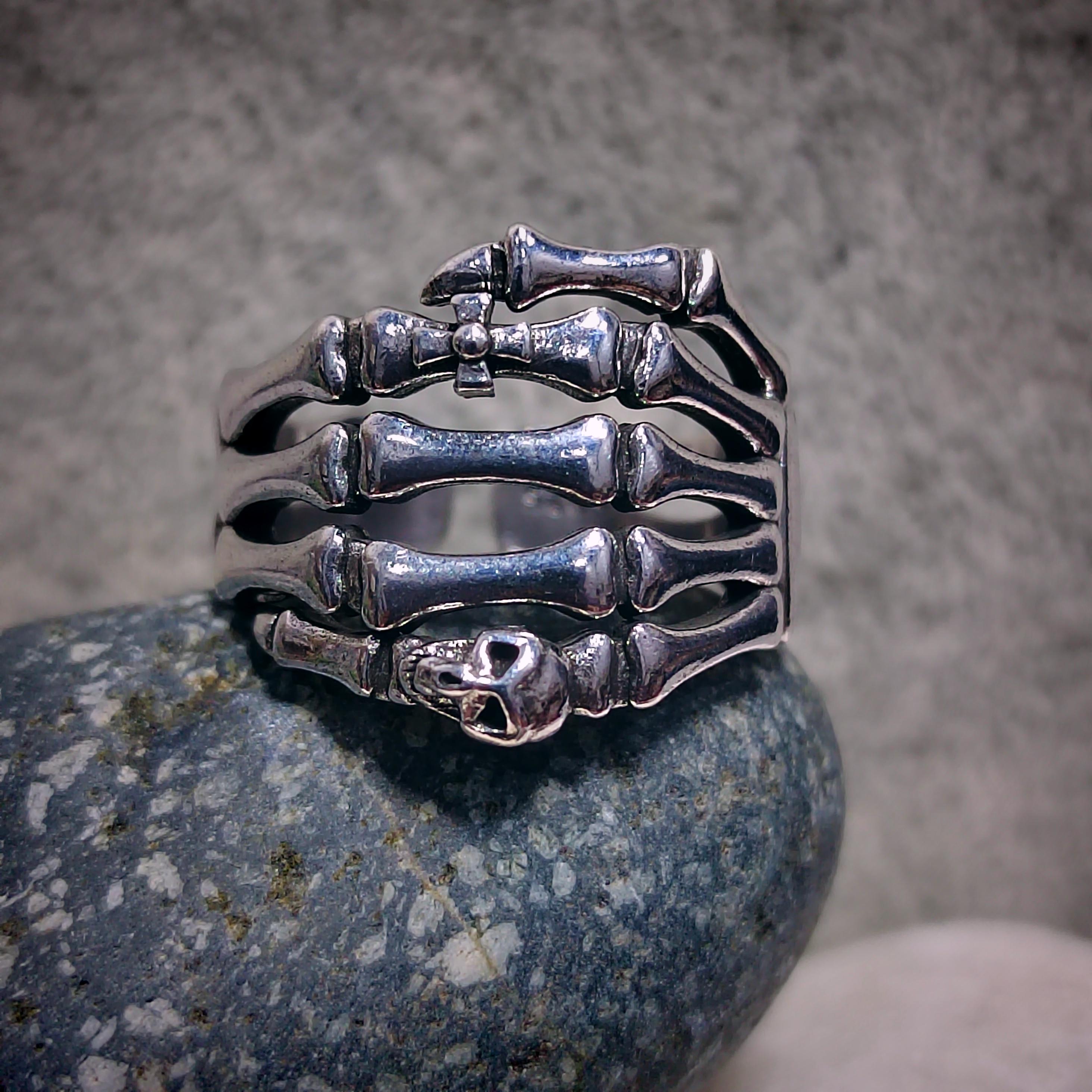 Silver skeleton hand ring on a textured stone surface with a neutral background