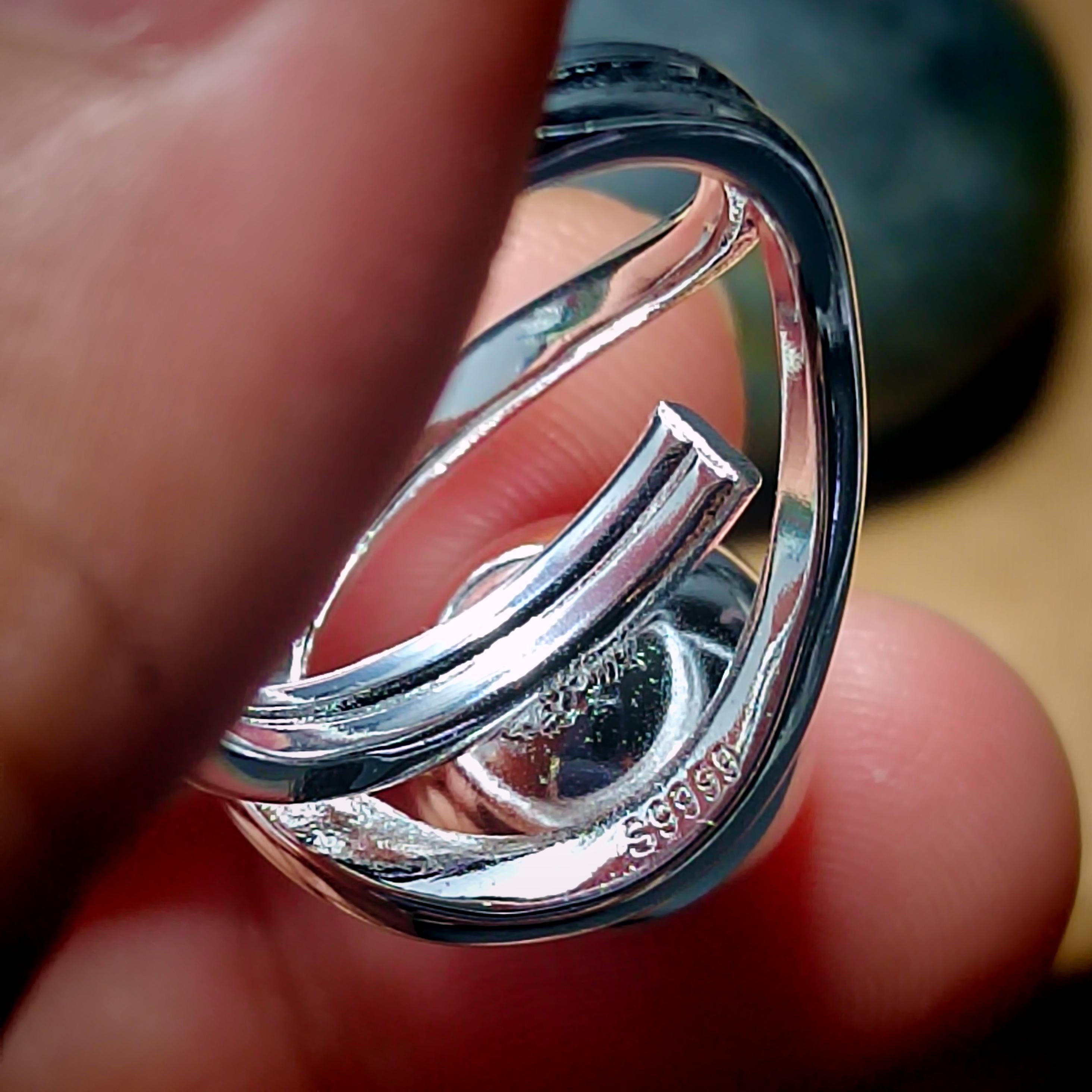 Silver ring held between fingers with '9999' stamp visible