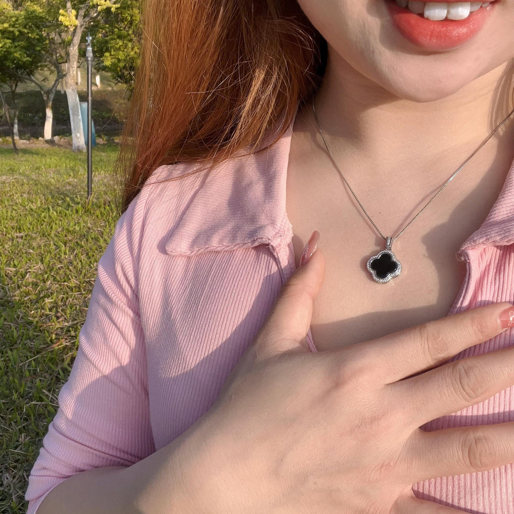 Person wearing a necklace with a black flower pendant outdoors