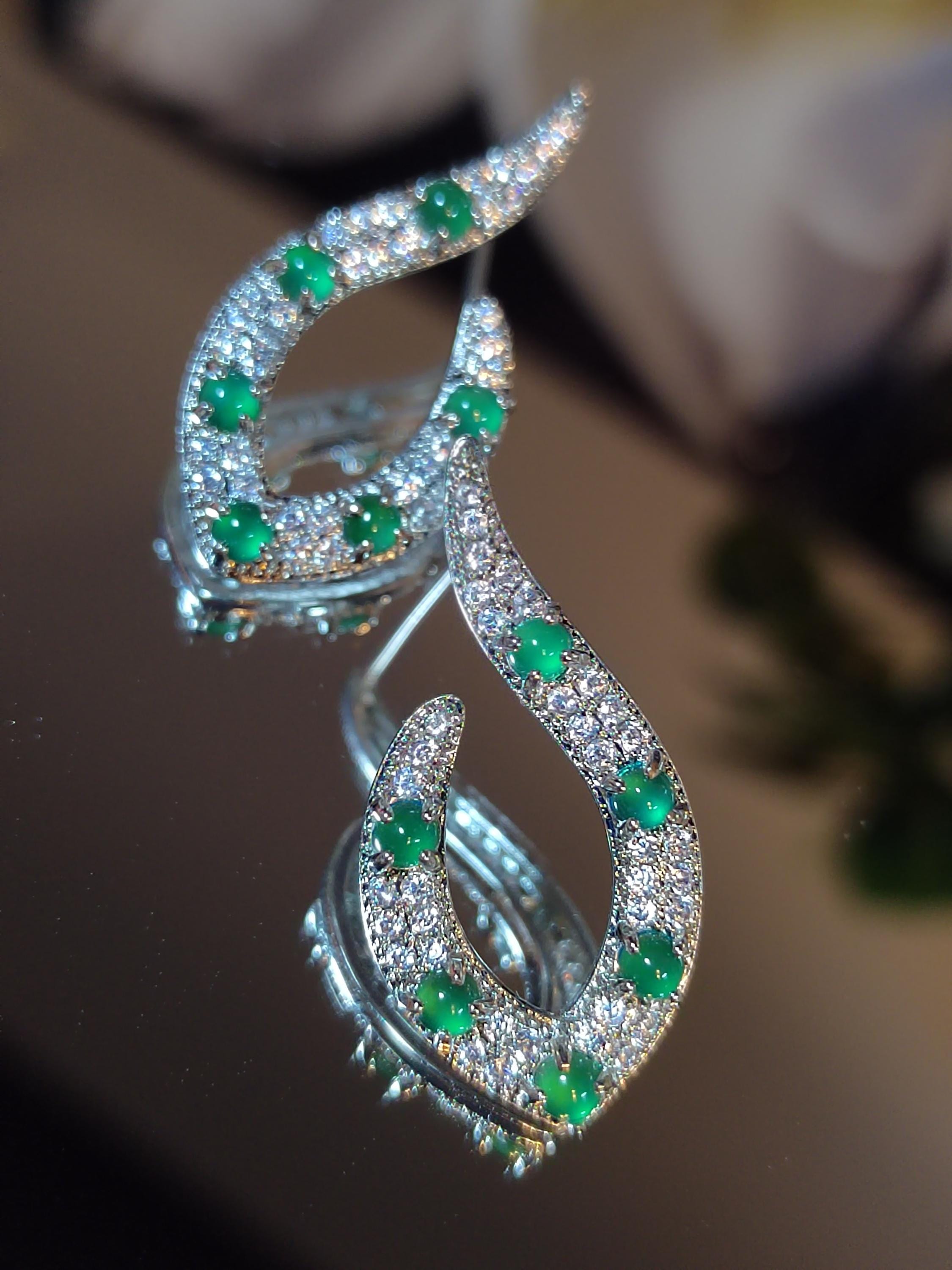 Elegant earrings with green gemstones and clear stones on a reflective surface