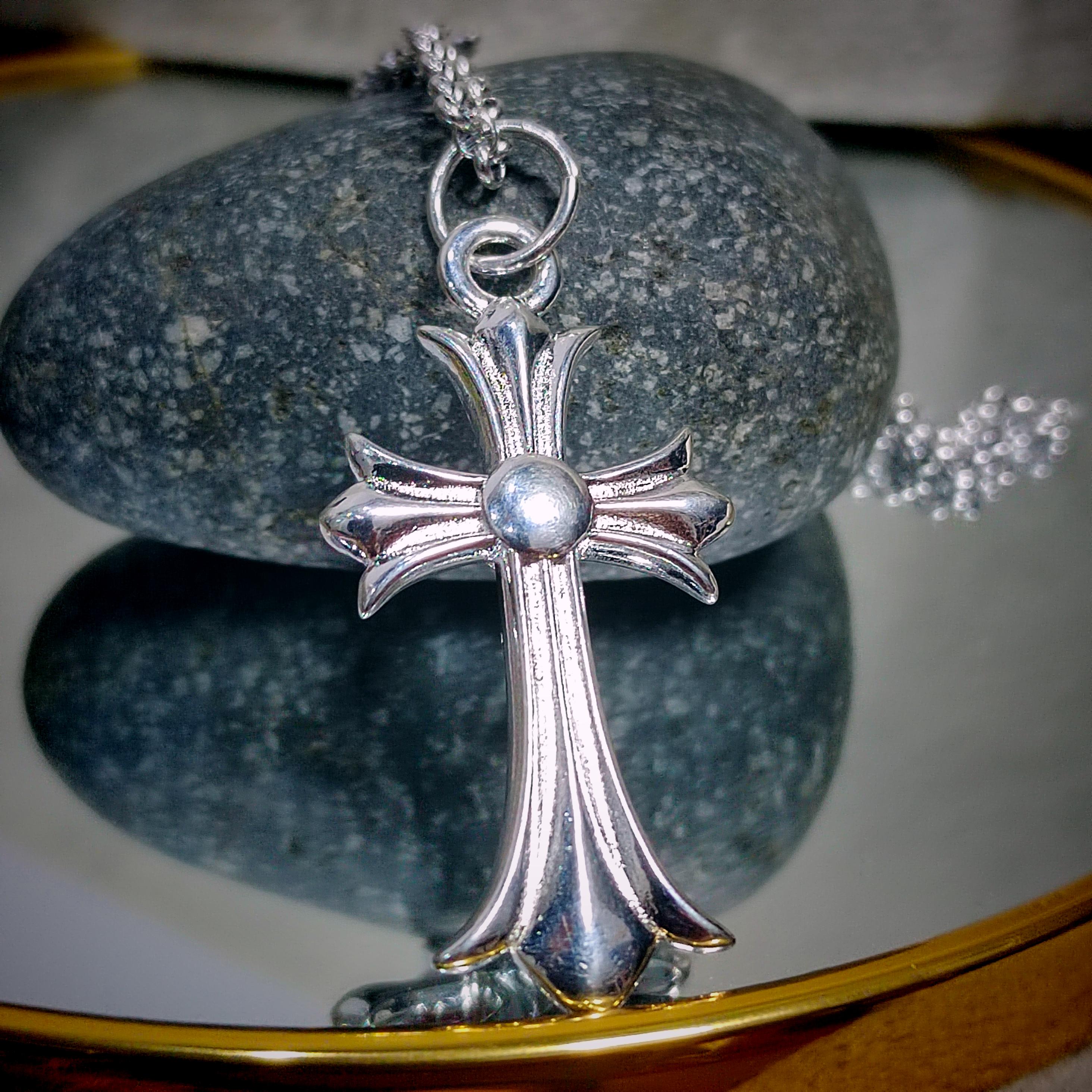 Silver cross pendant on a chain against a reflective surface with a stone background