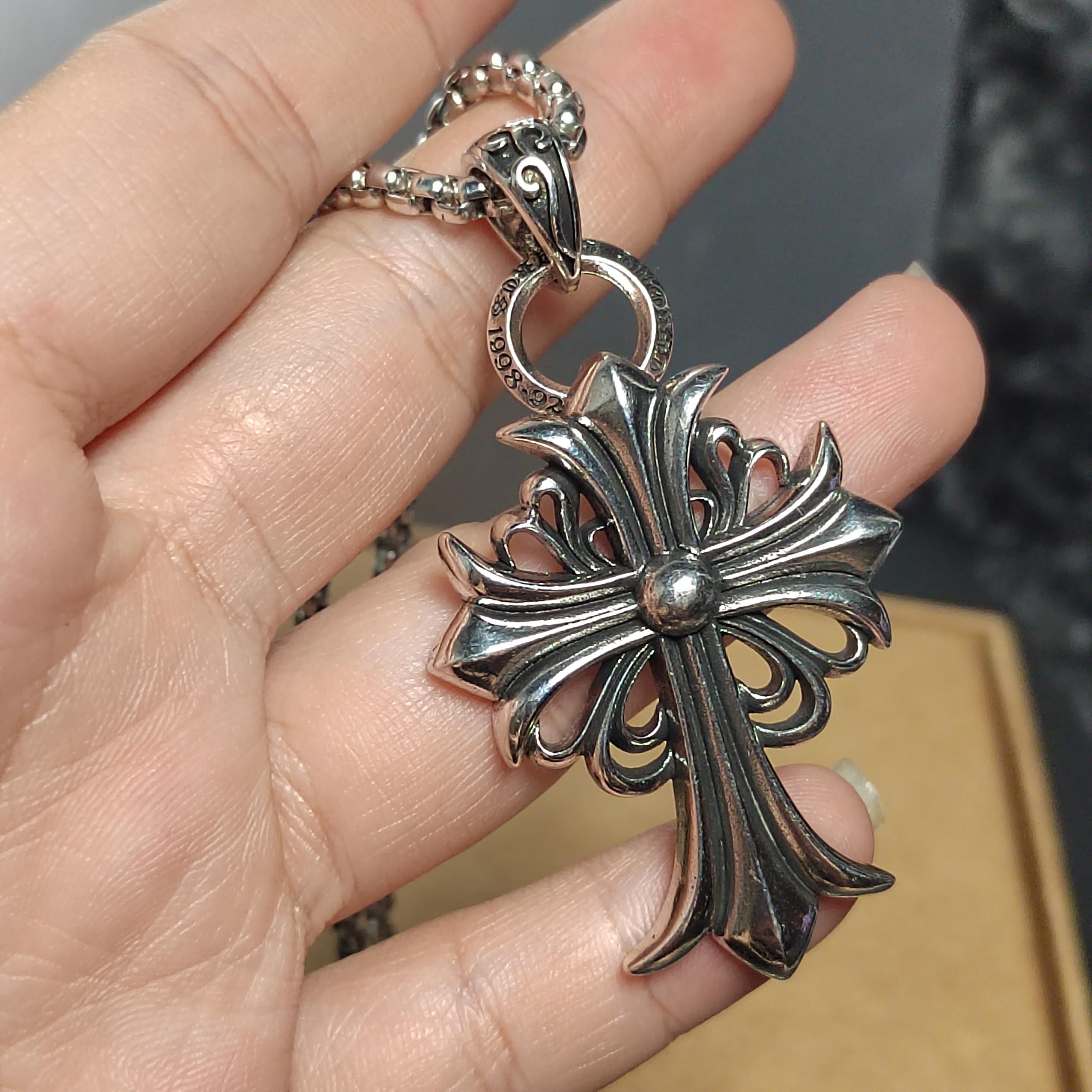 Silver cross pendant held in a hand with a blurred background