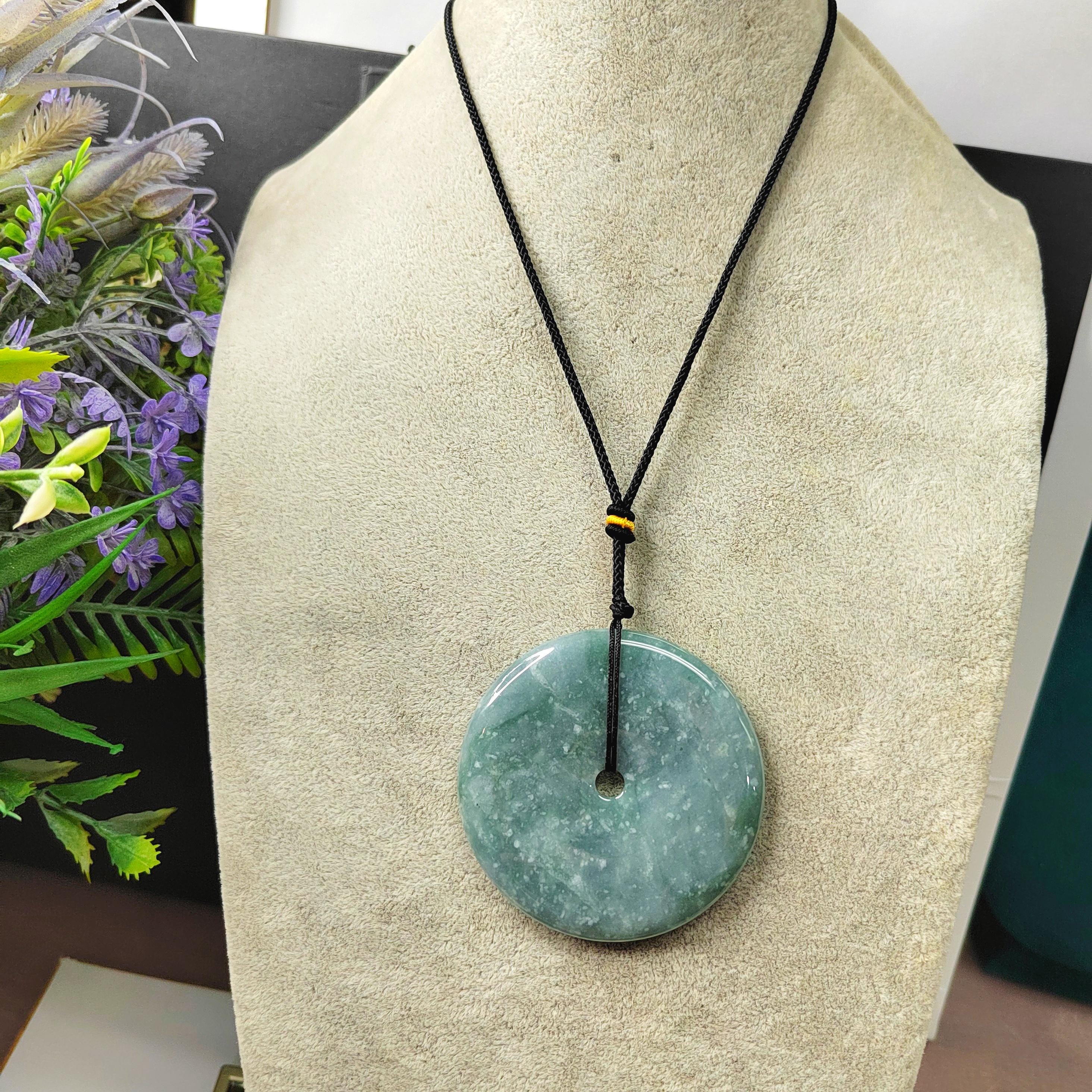 Green jade pendant necklace on a mannequin bust with flowers in the background