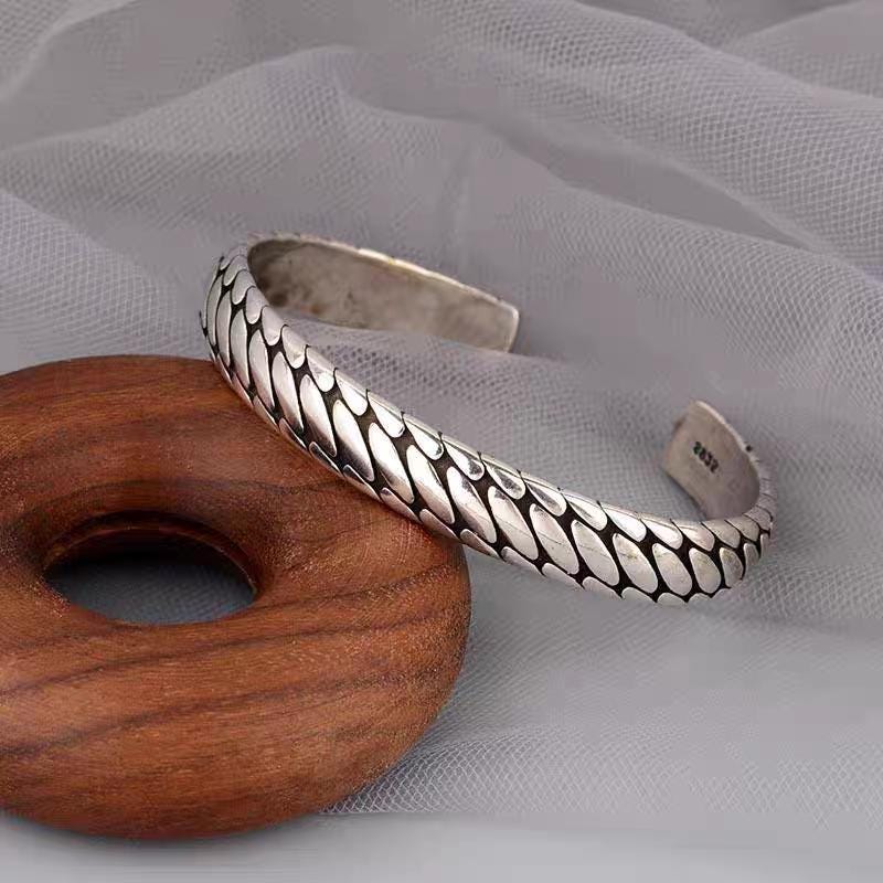 Silver bracelet with textured design on a wooden ring against a gray fabric background
