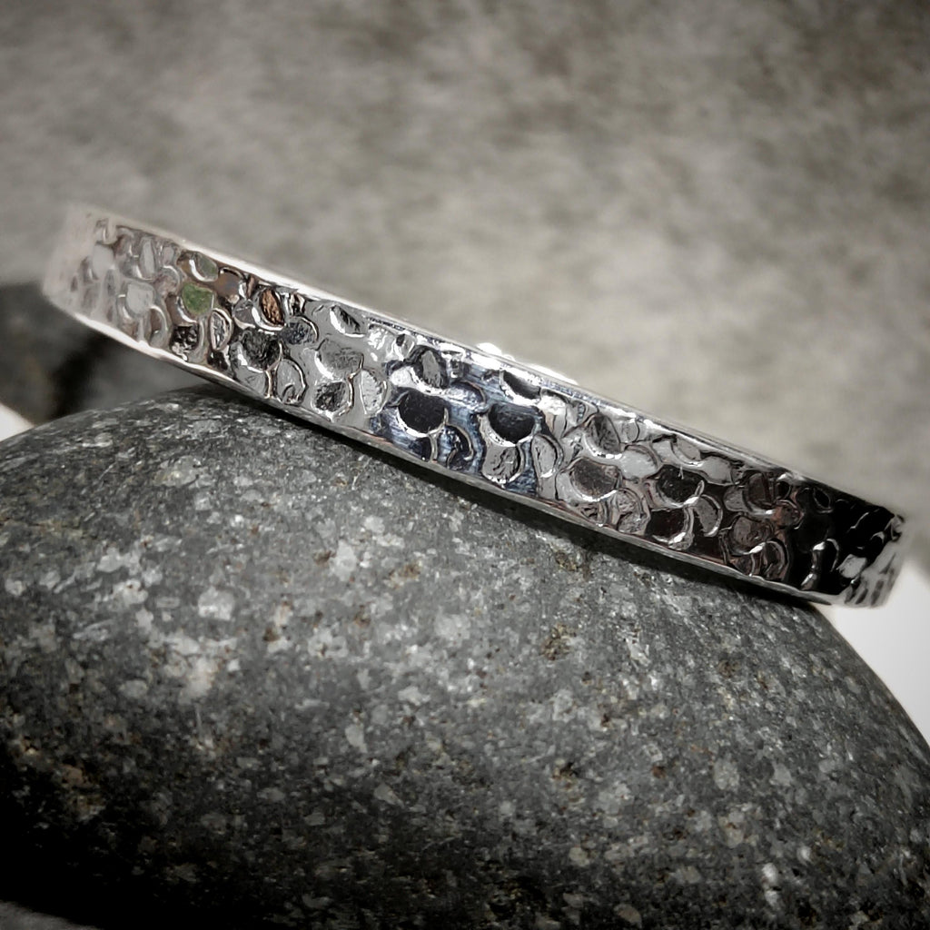 Silver bracelet with a textured pattern on a gray stone surface
