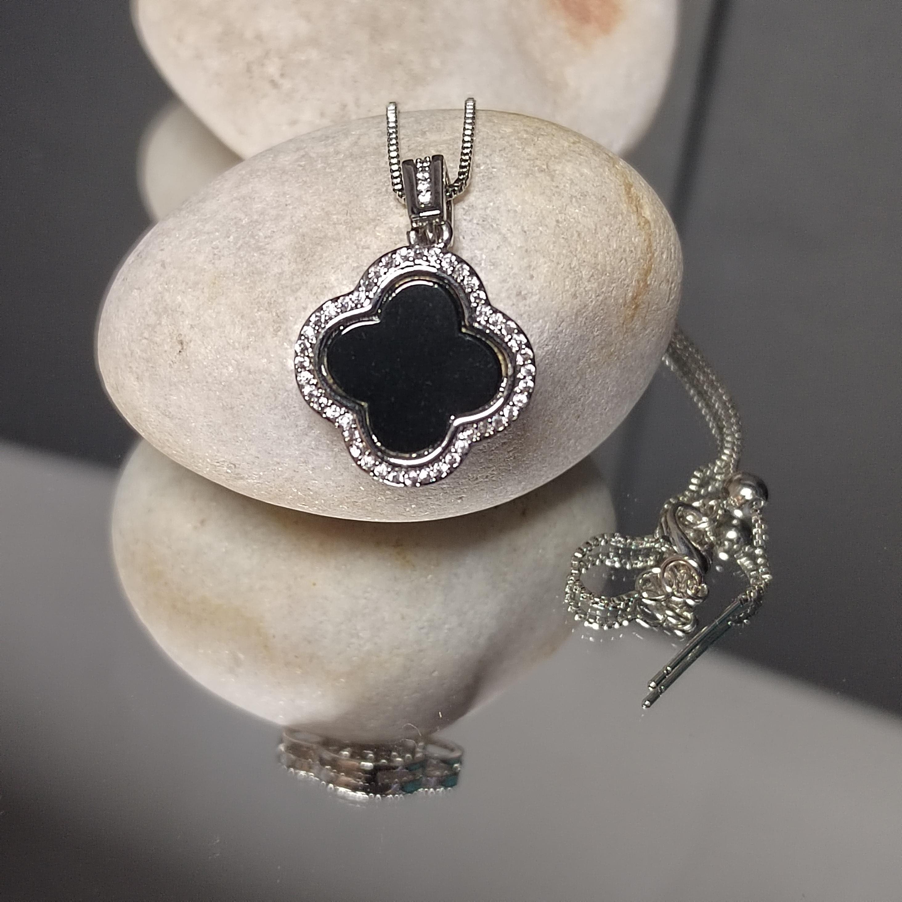 Silver necklace with a black floralclover pendant on a reflective surface