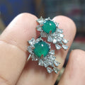 Close-up of elegant apple green jadeite earrings with white gold plating and sparkling zirconia accents held between fingers.