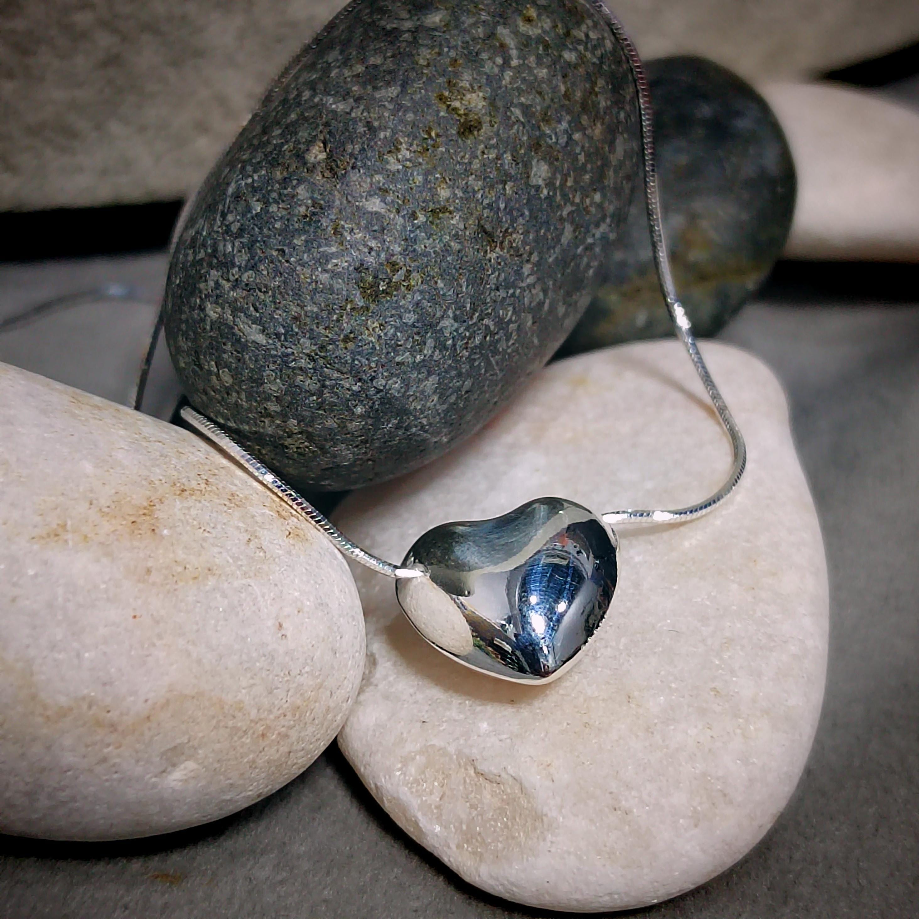 Silver heart-shaped pendant on a chain lying on stones