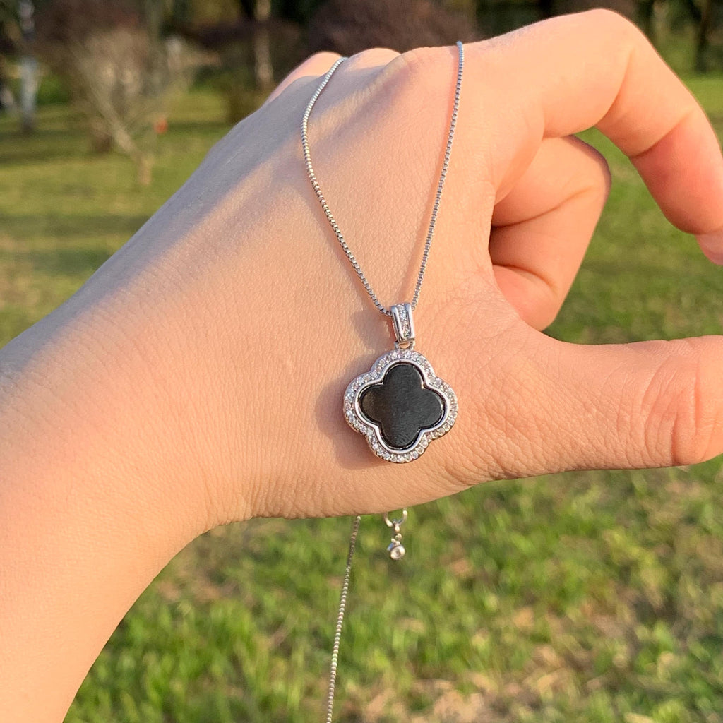 Hand holding a necklace with a clover-shaped pendant against a blurred outdoor background