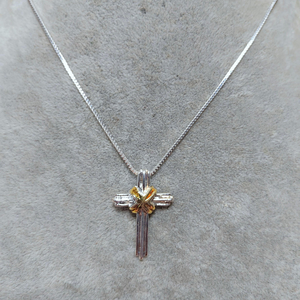 Silver cross necklace with a small yellow gemstone on a gray surface