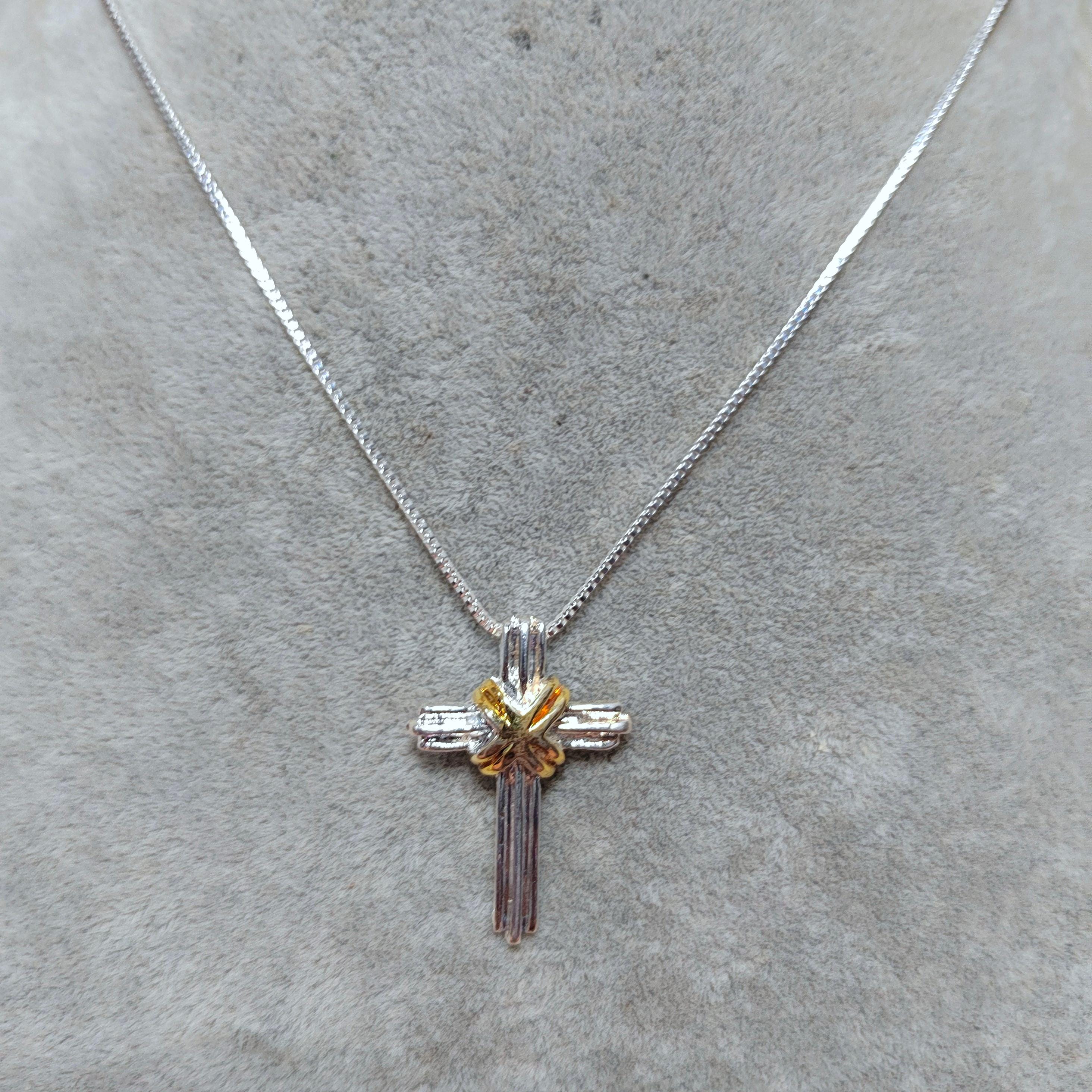 Silver cross necklace with a small yellow gemstone on a gray surface
