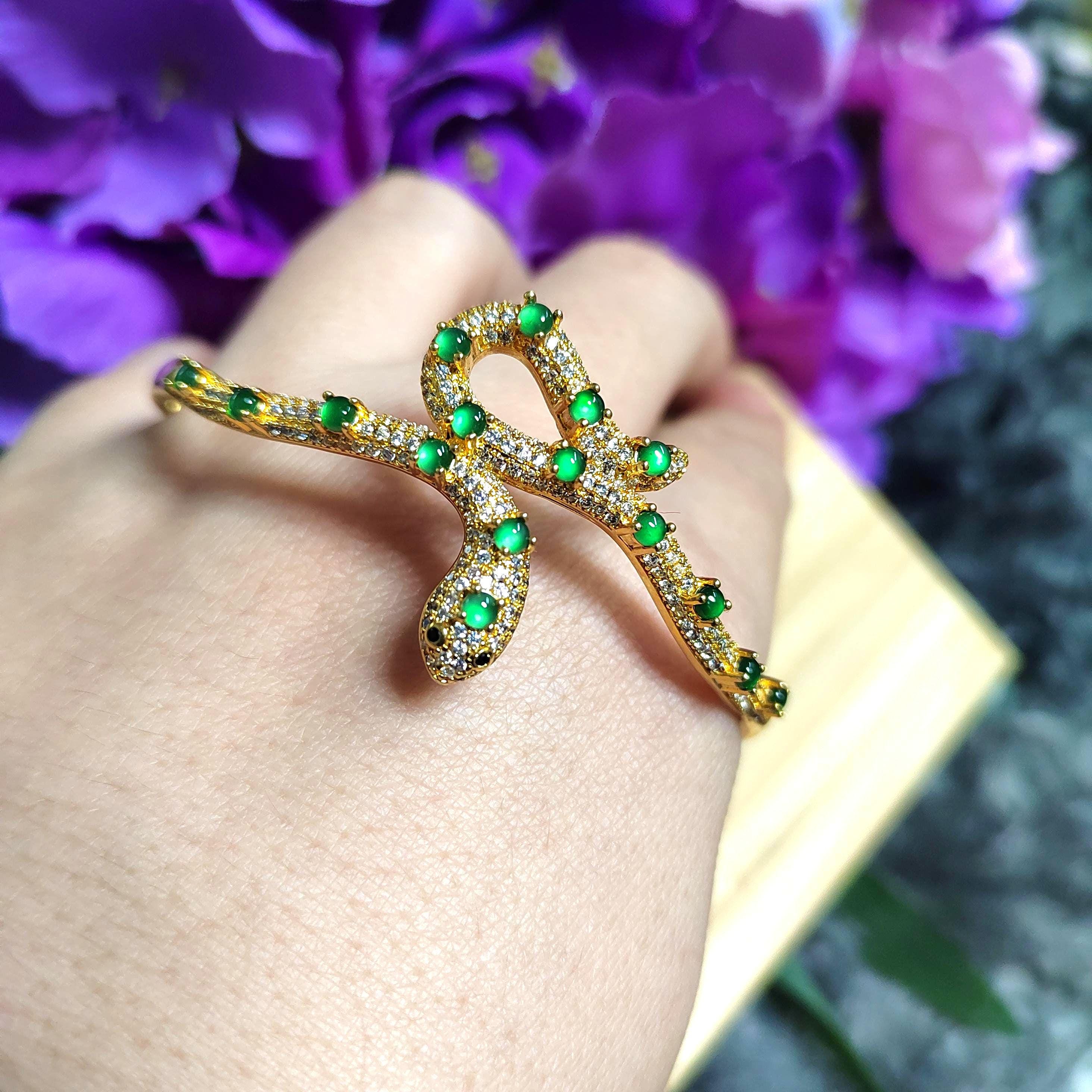 Gold ring with green gemstones on a hand against a purple floral background