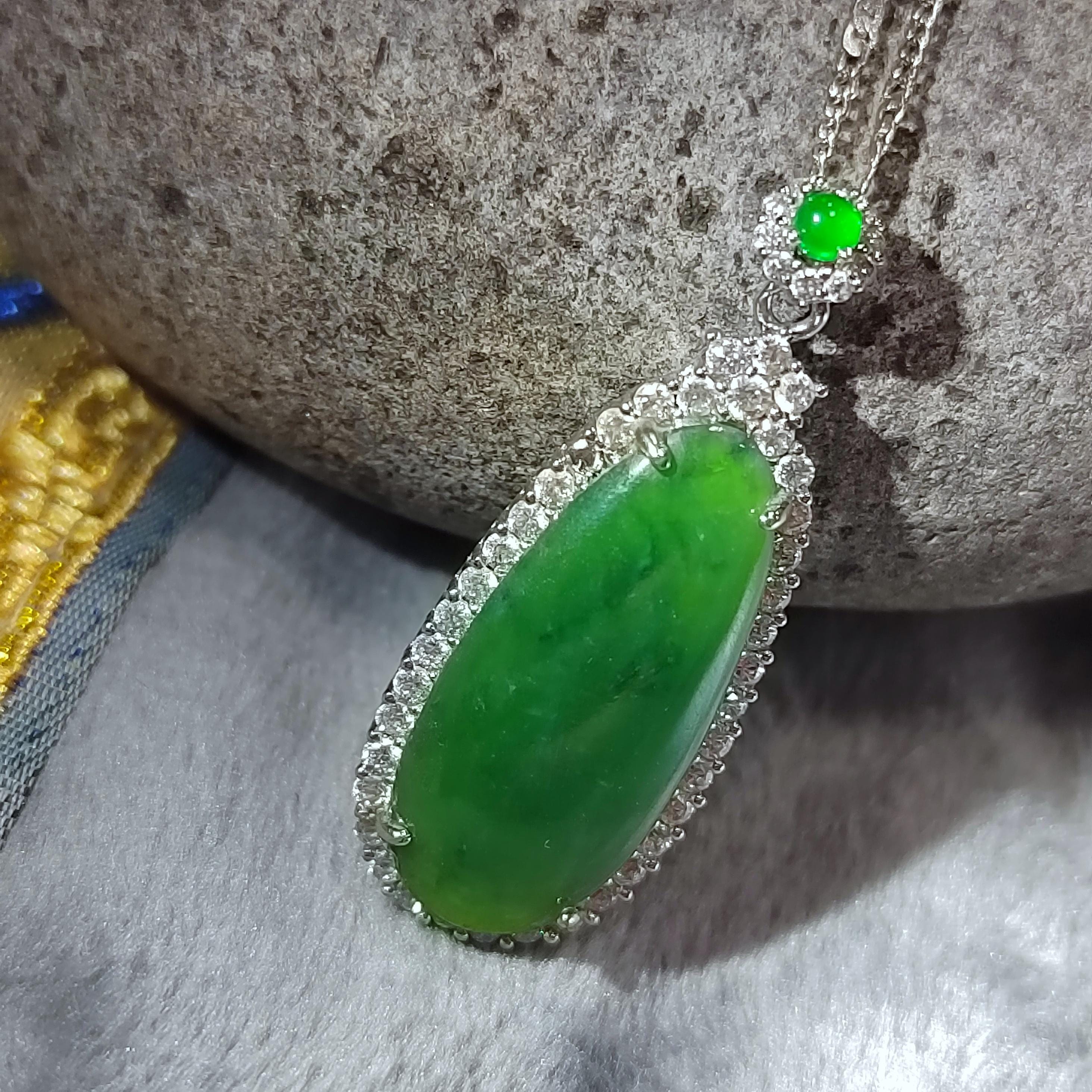 Green jade pendant with silver frame on a stone surface