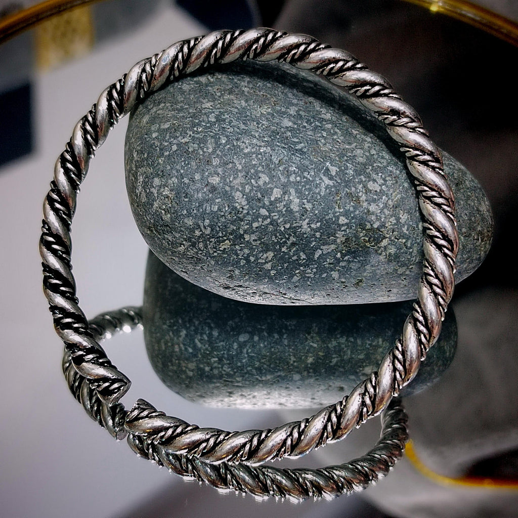 Silver bracelet with twisted design on a reflective surface with a stone background
