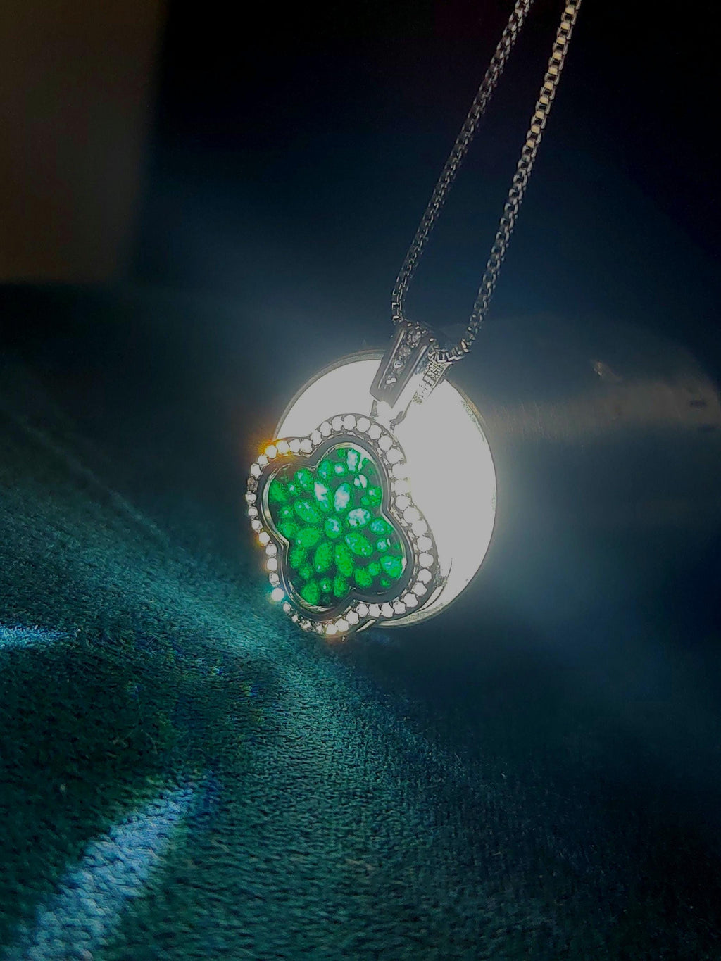 Silver necklace with a green floralclover pendant on a dark fabric background