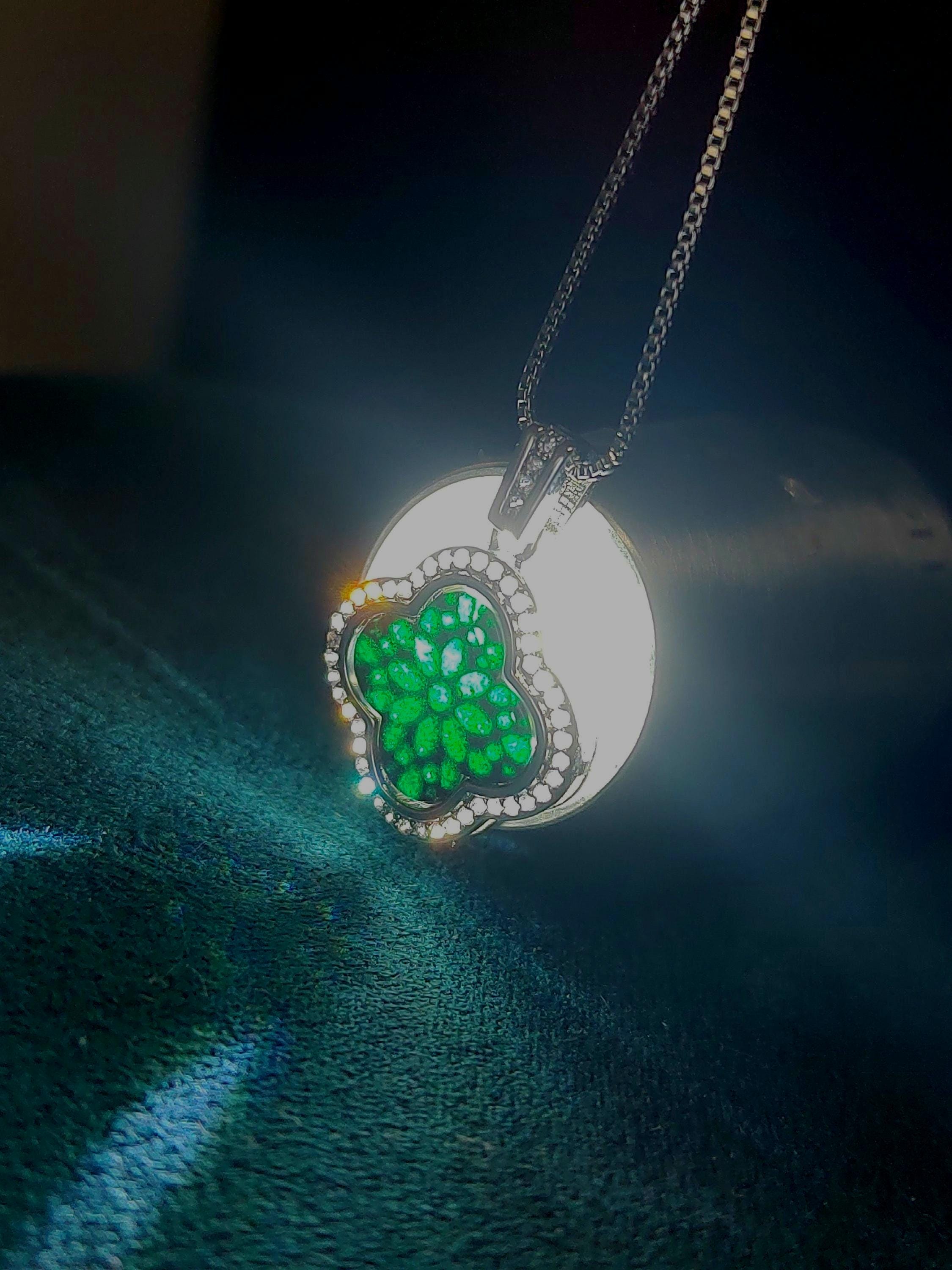 Silver necklace with a green floralclover pendant on a dark fabric background