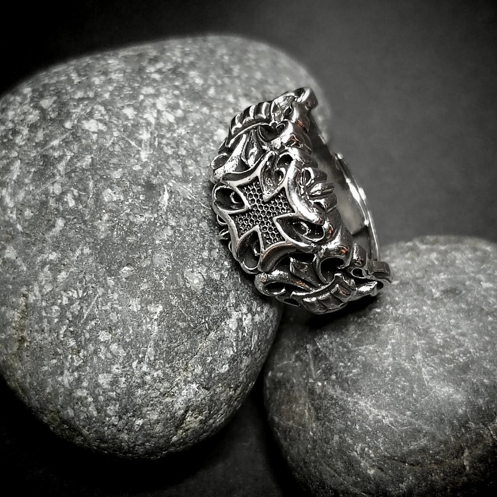 Silver ring with ornate design on gray rocks.