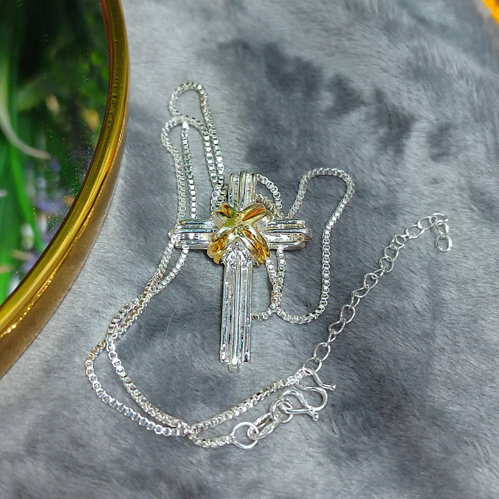 Silver cross necklace with a yellow center on a gray surface