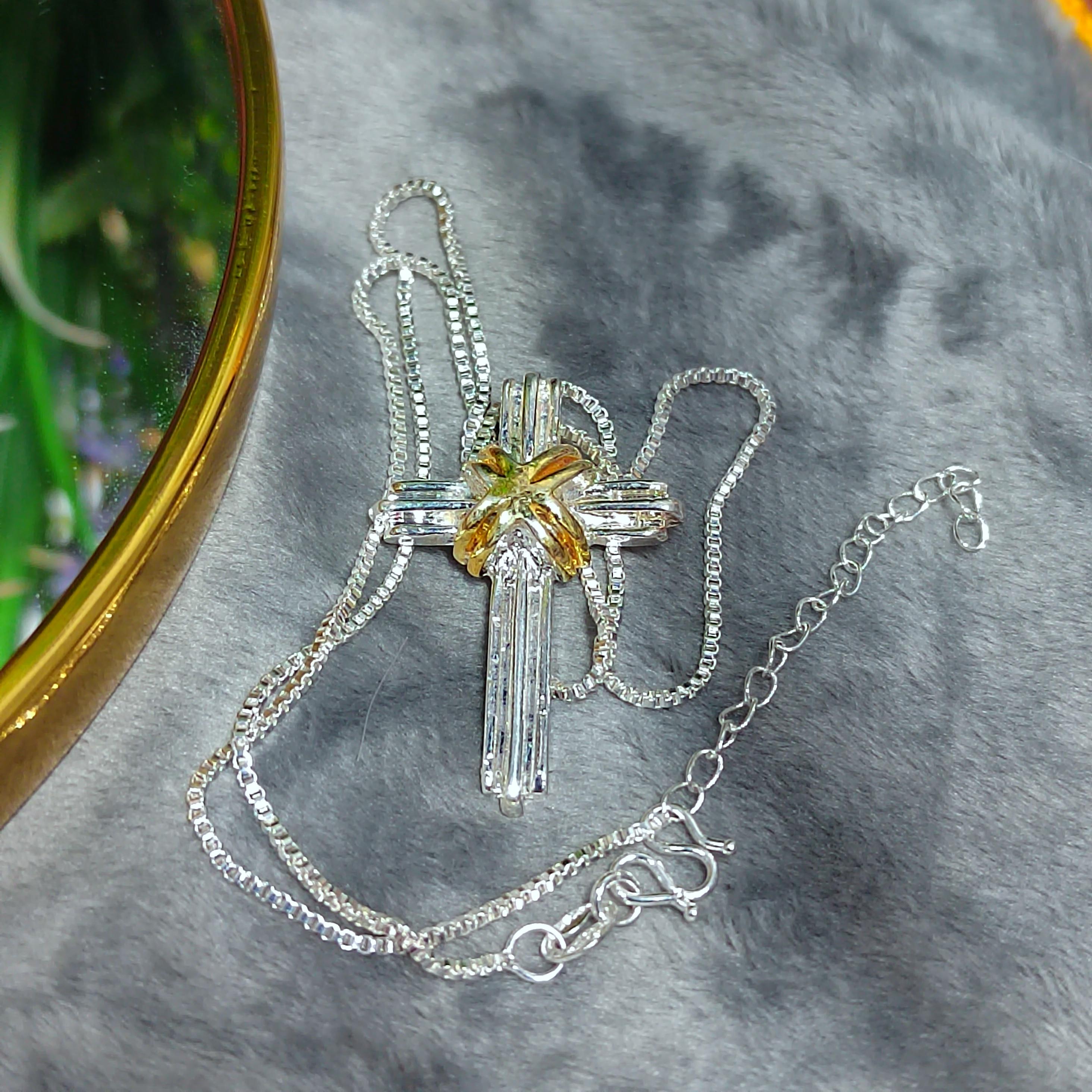 Silver cross necklace with a yellow center on a gray surface