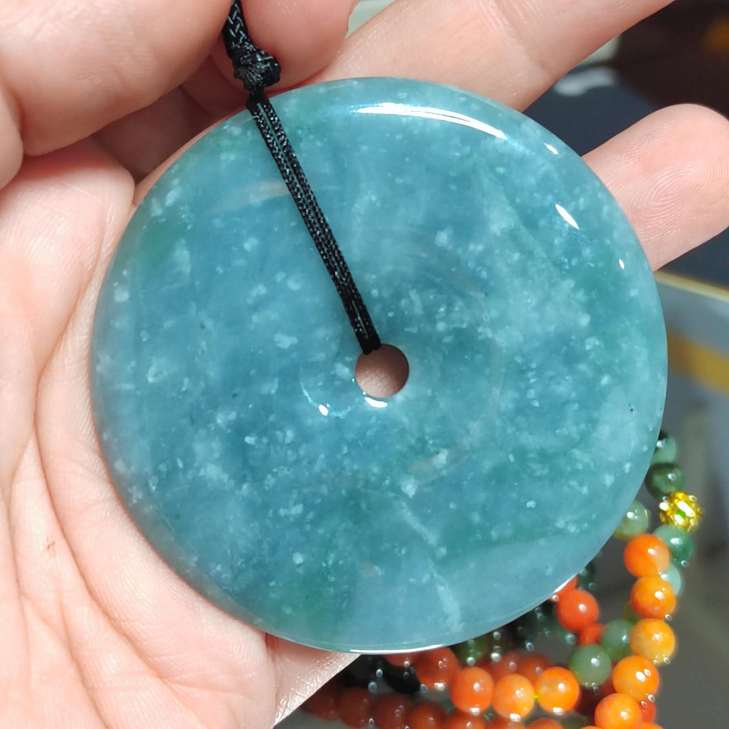 Turquoise jade pendant held in a hand with blurred beads in the background