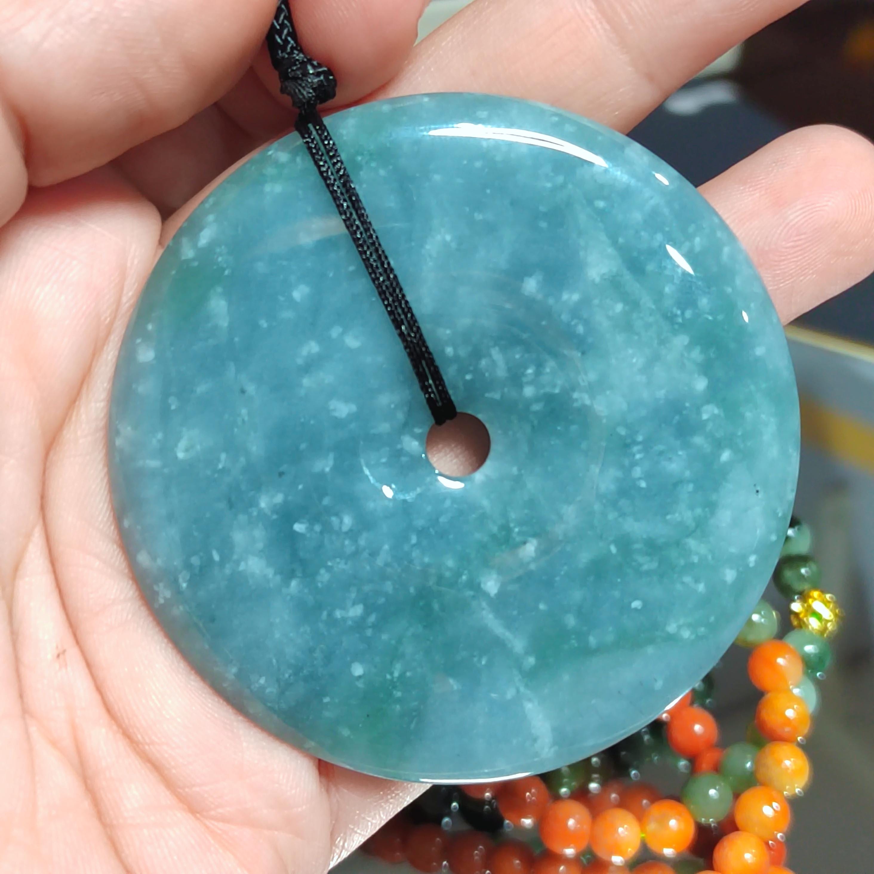 Turquoise jade pendant held in a hand with blurred beads in the background