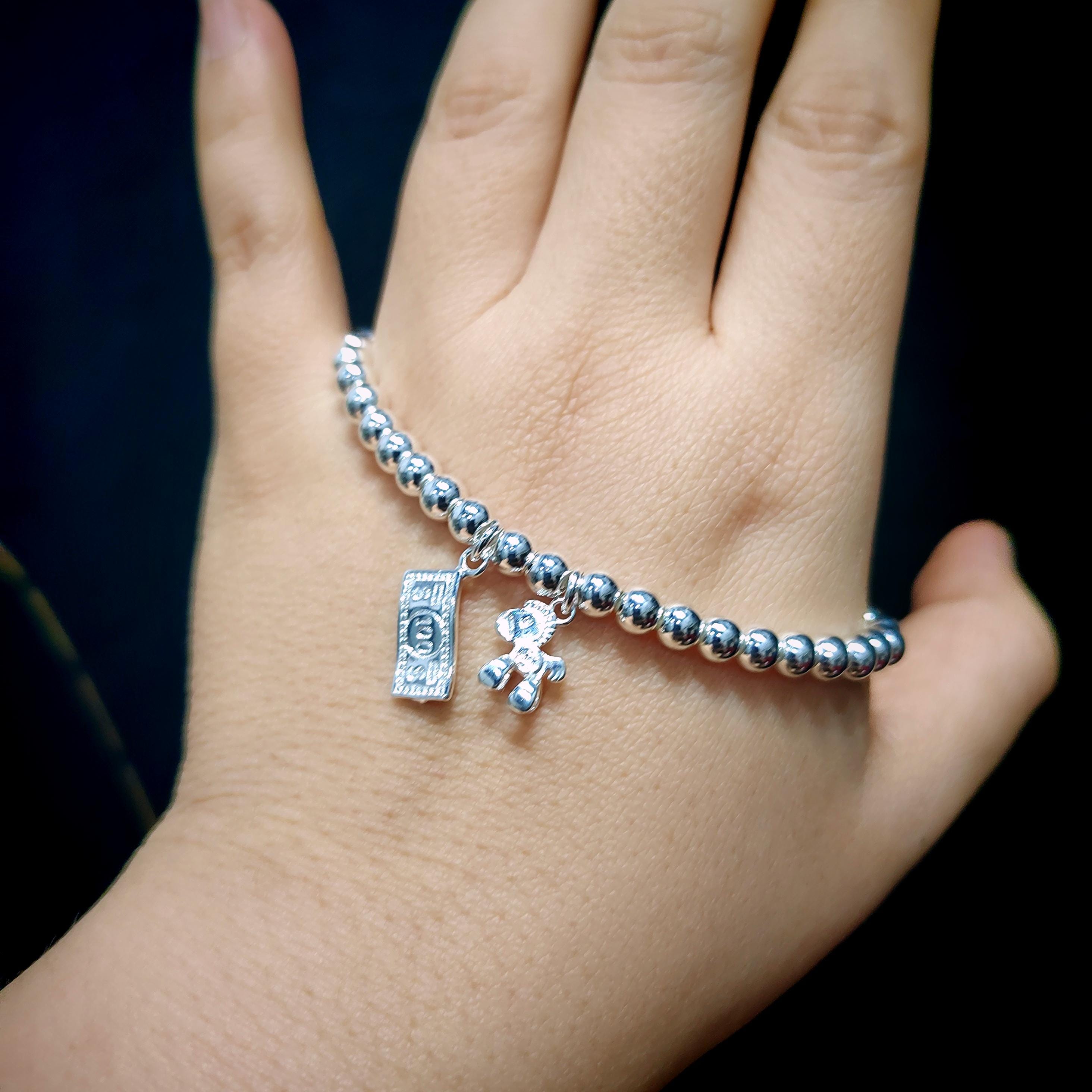 Silver beaded bracelet with charms on a hand against a dark background
