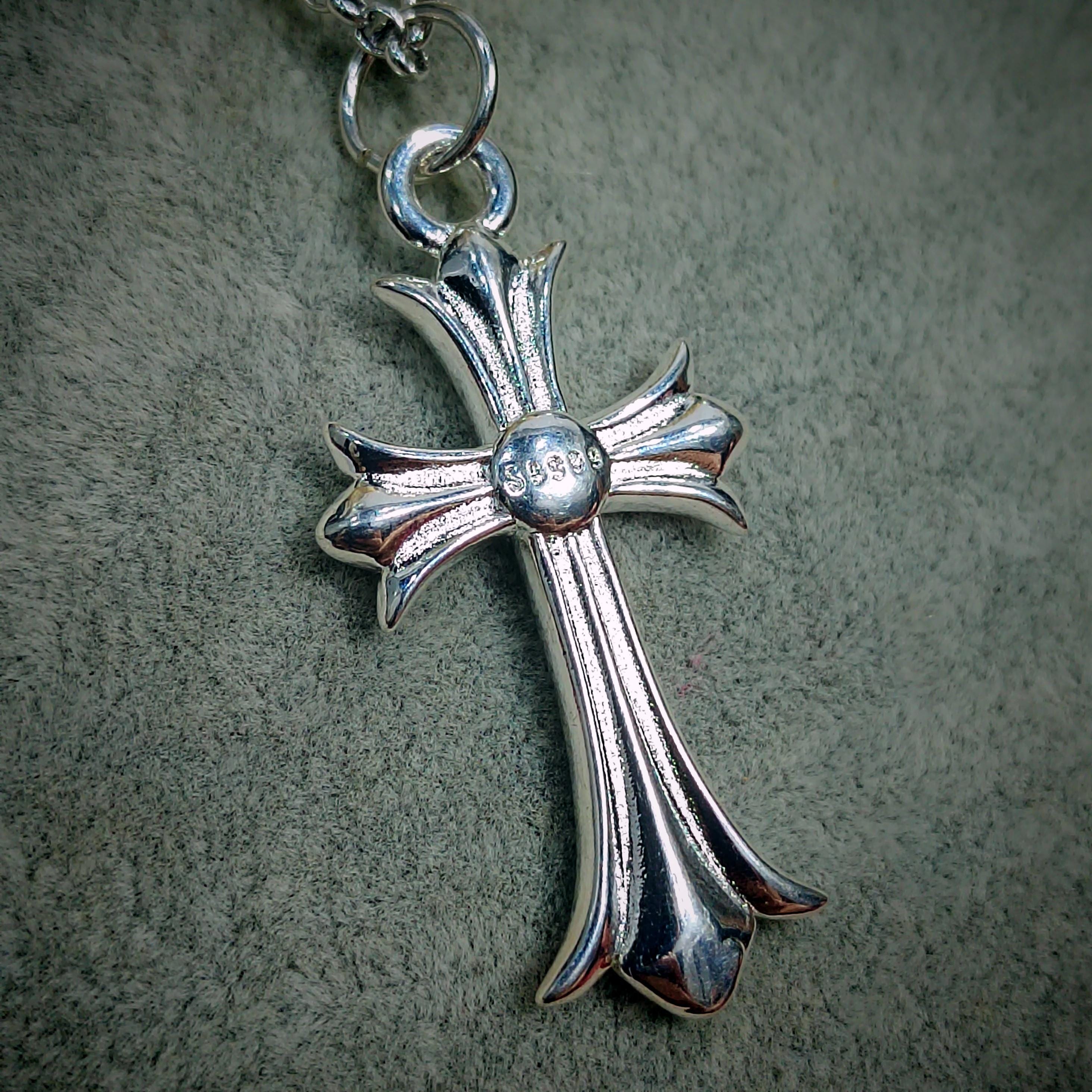Silver cross pendant on a chain against a textured gray background