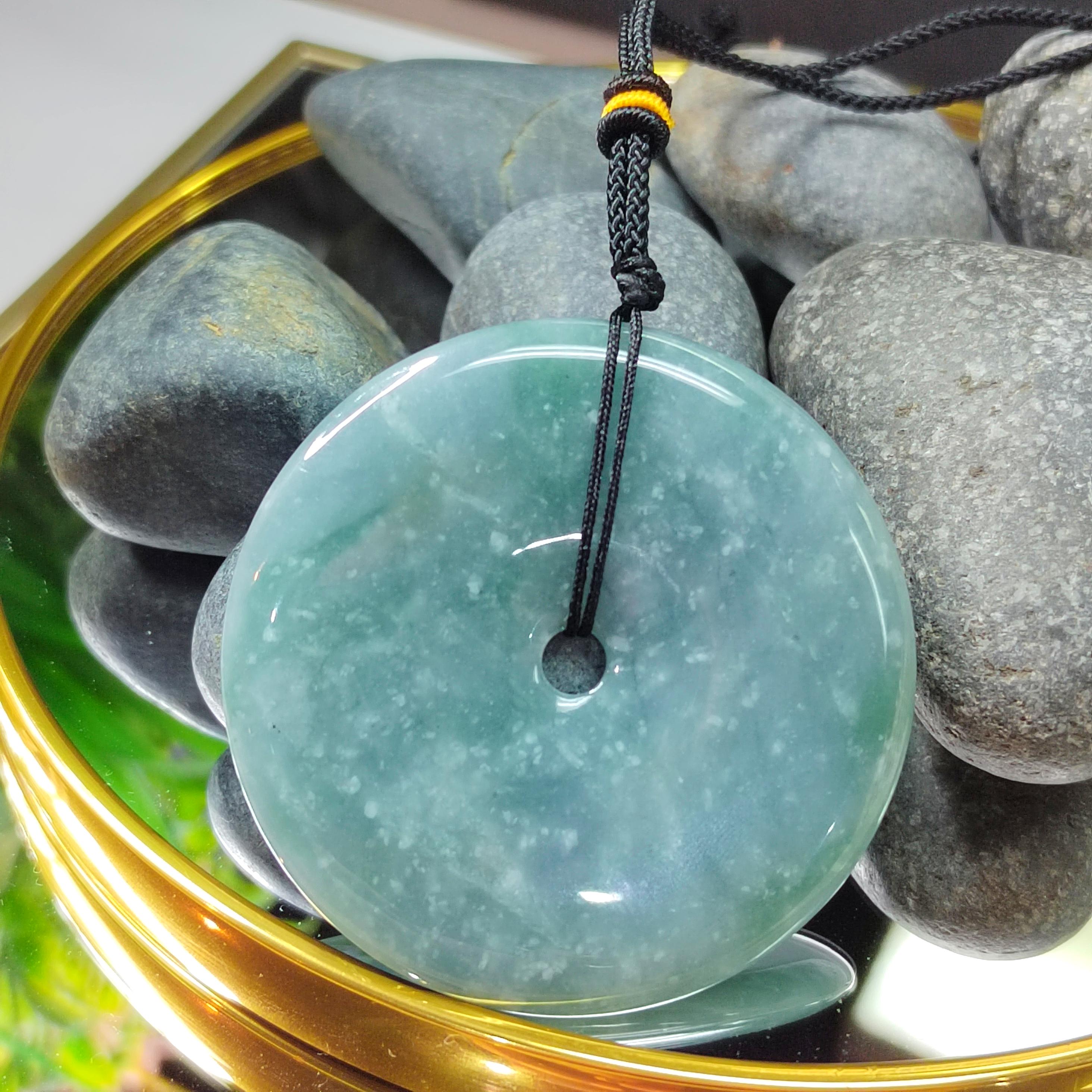 Green jade pendant on a black cord with stones in the background