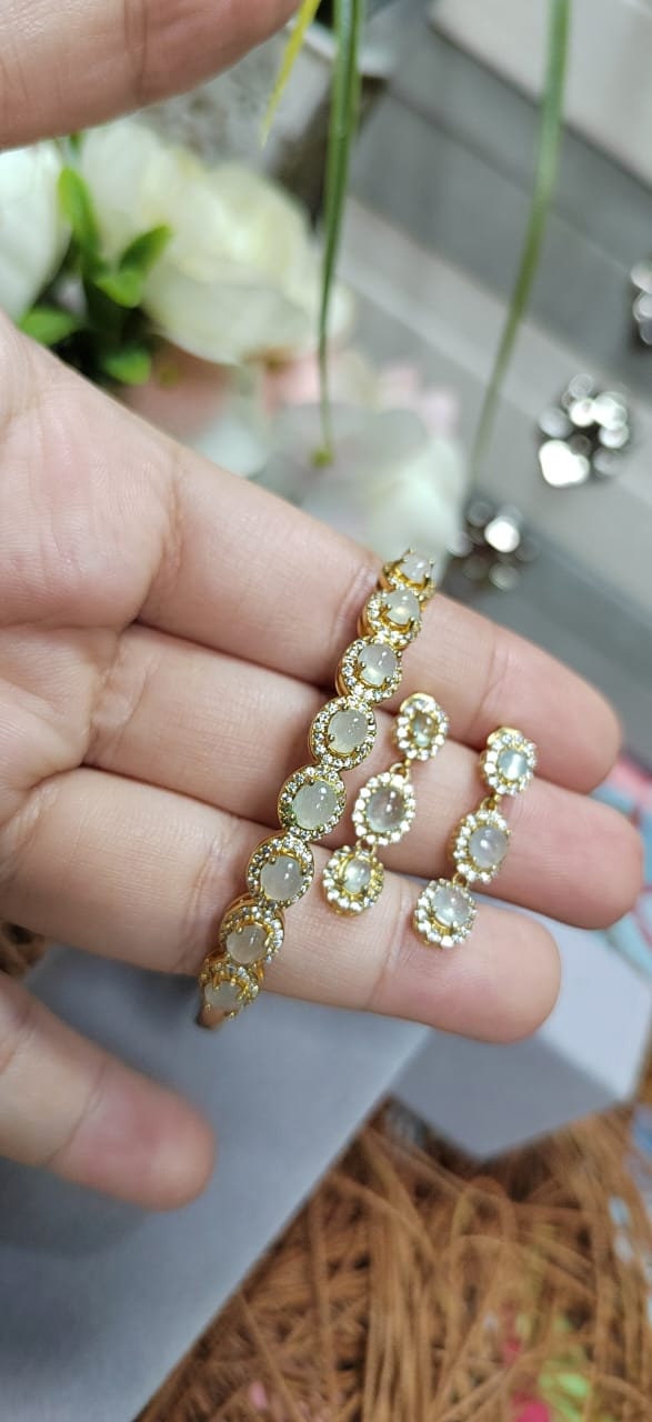 Gold earrings with clear stones held between fingers against a blurred background