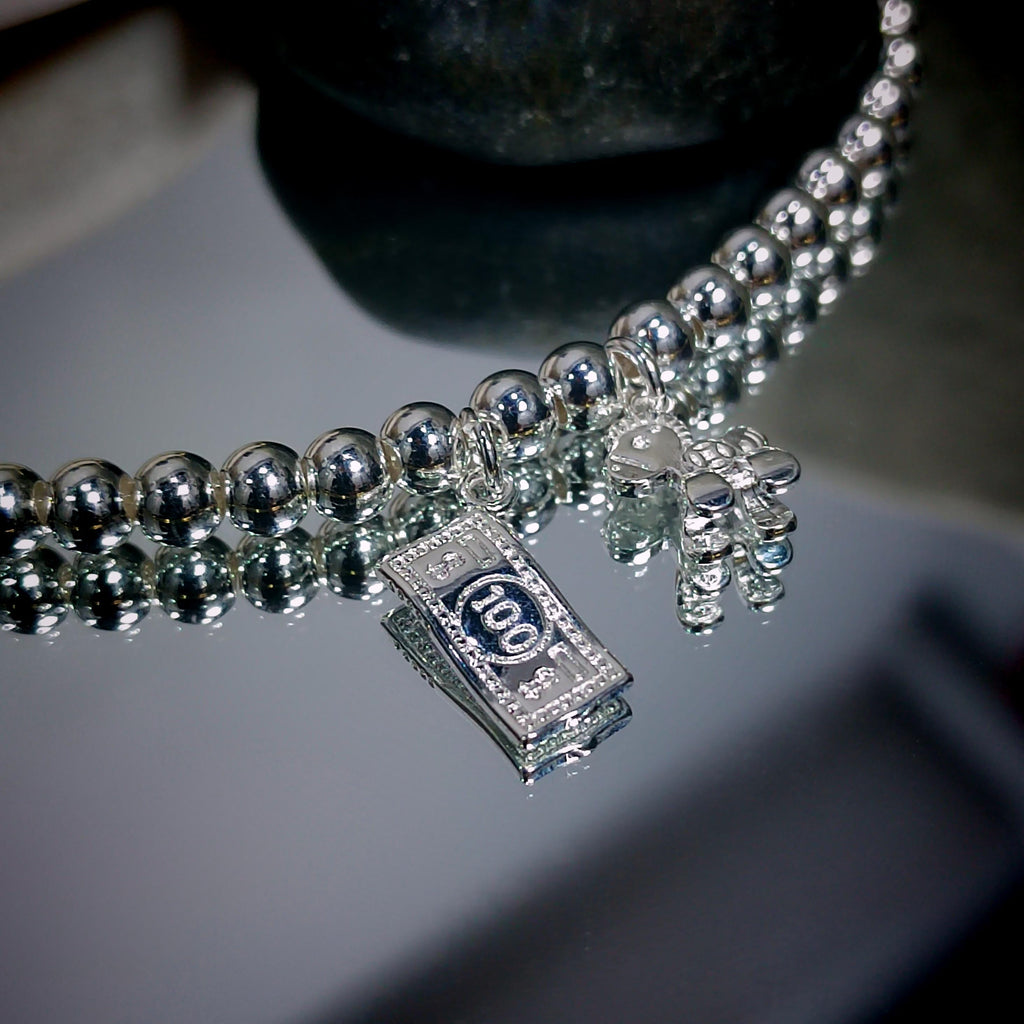Silver beaded necklace with a '100' pendant on a reflective surface