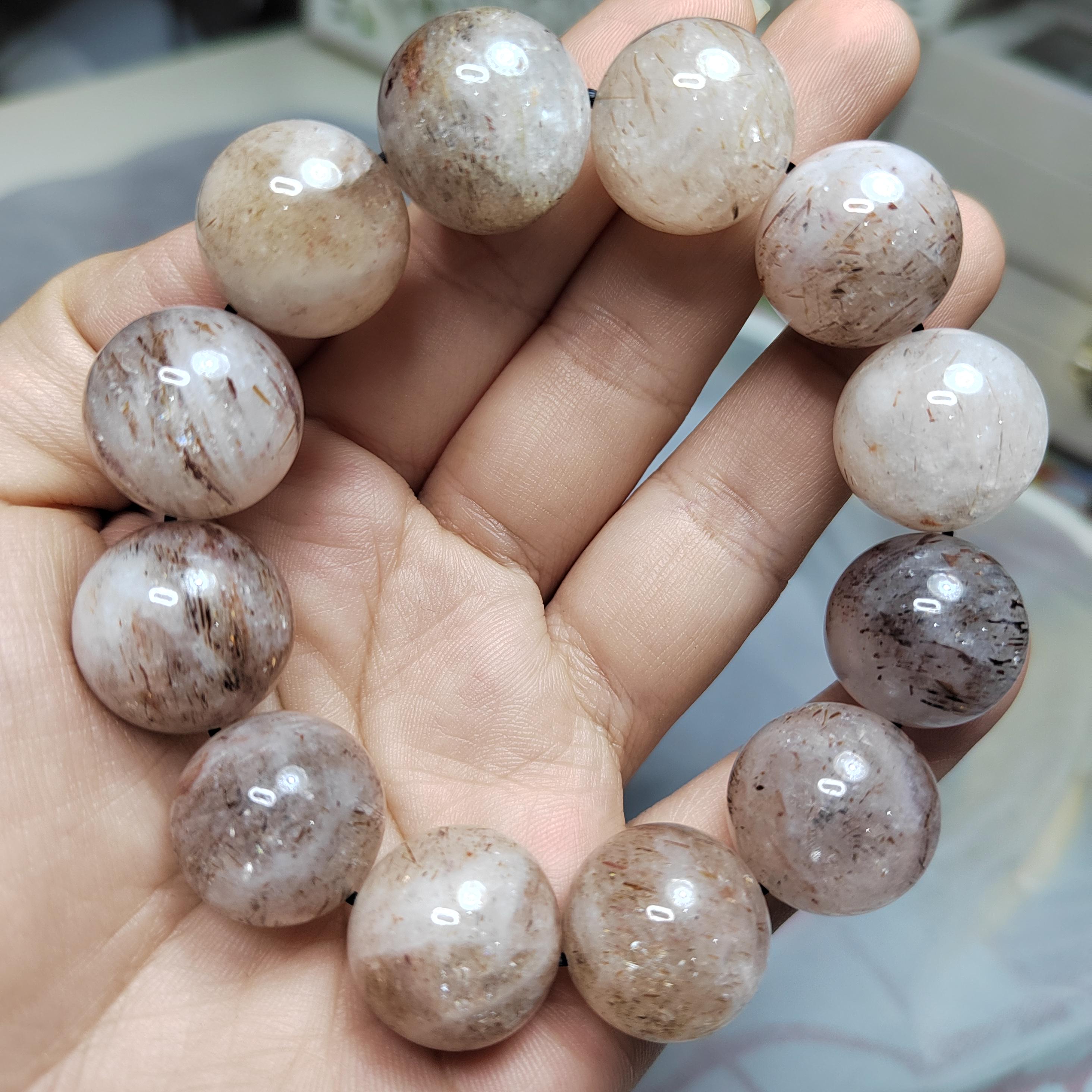 May include: A bracelet made of round, translucent, light brown and white beads with dark brown streaks. The beads are strung together with a black cord.