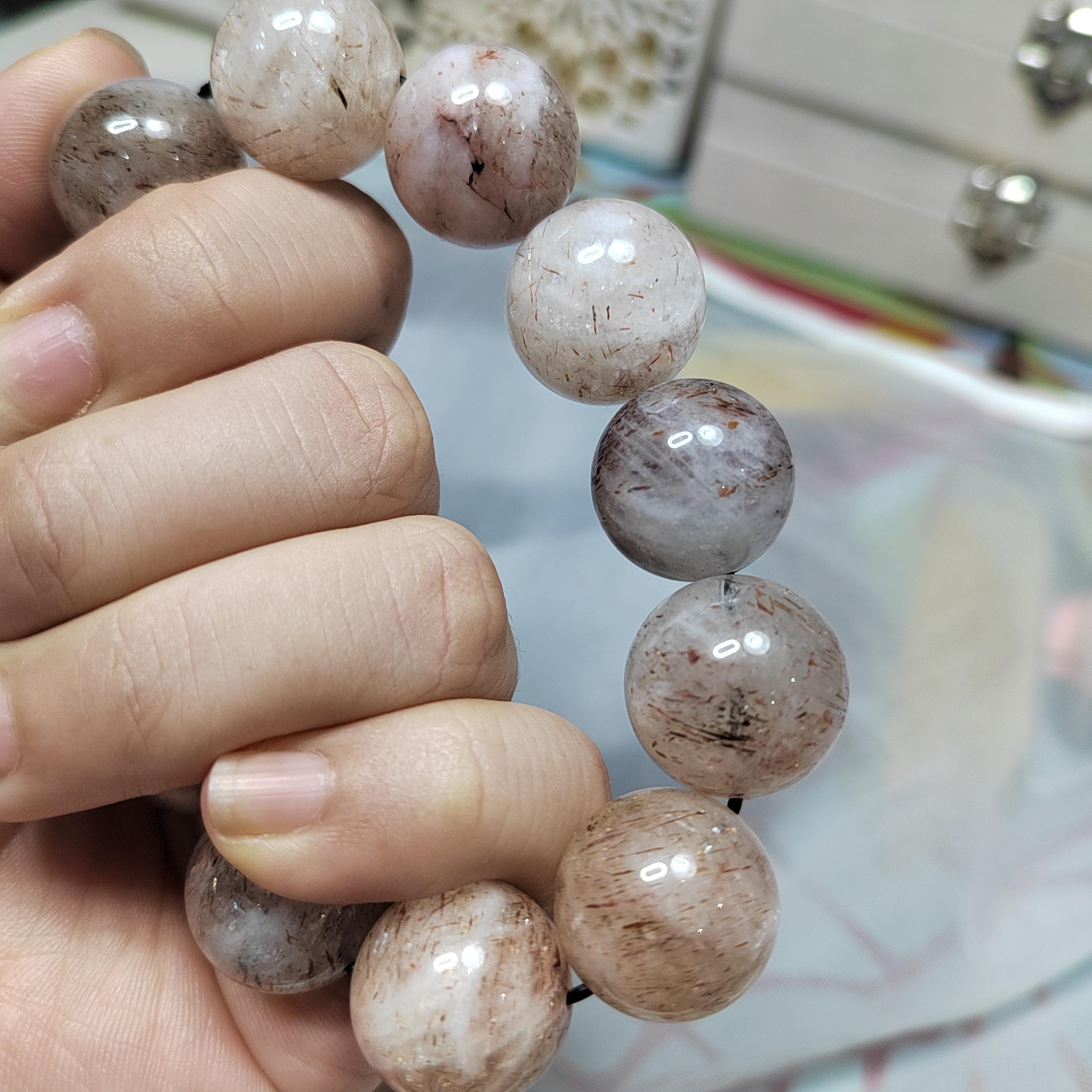 Hand holding a bracelet with round, beige beads against a blurred background
