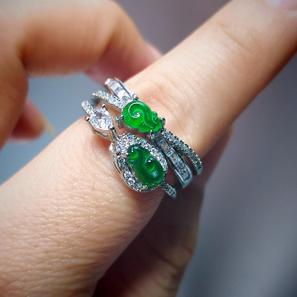 Two green gemstone rings with silver settings on a finger against a blurred background