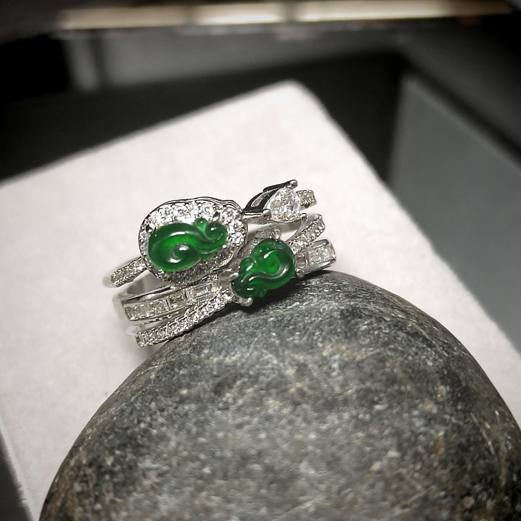 Silver ring with green gemstones on a stone surface