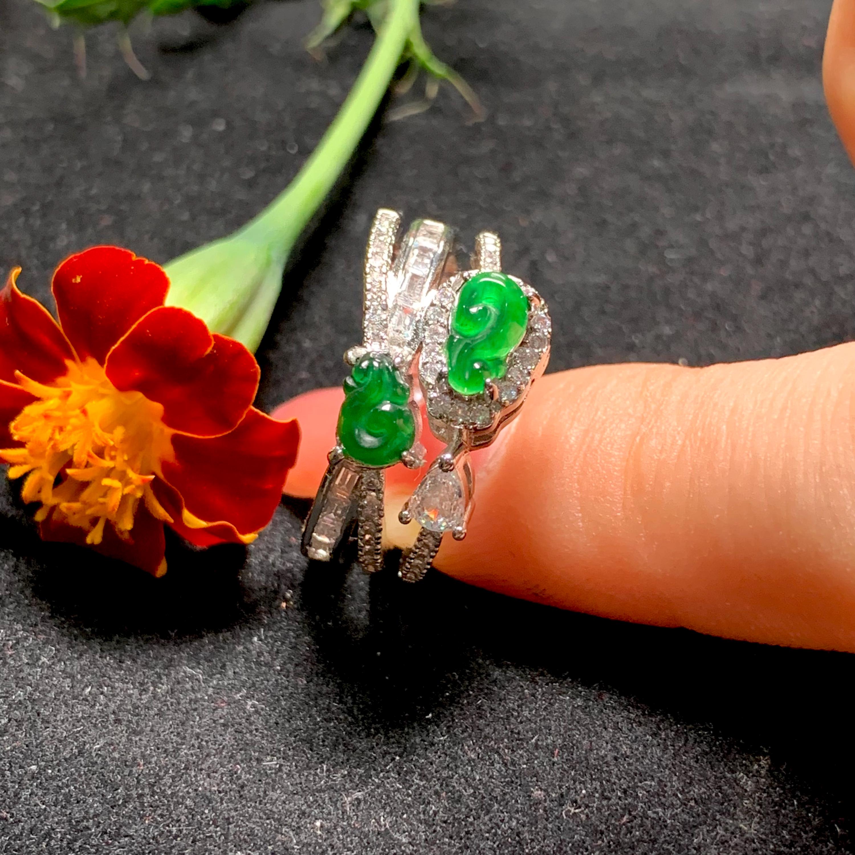 Jewelry with green gemstones held between fingers next to a red flower on a dark surface