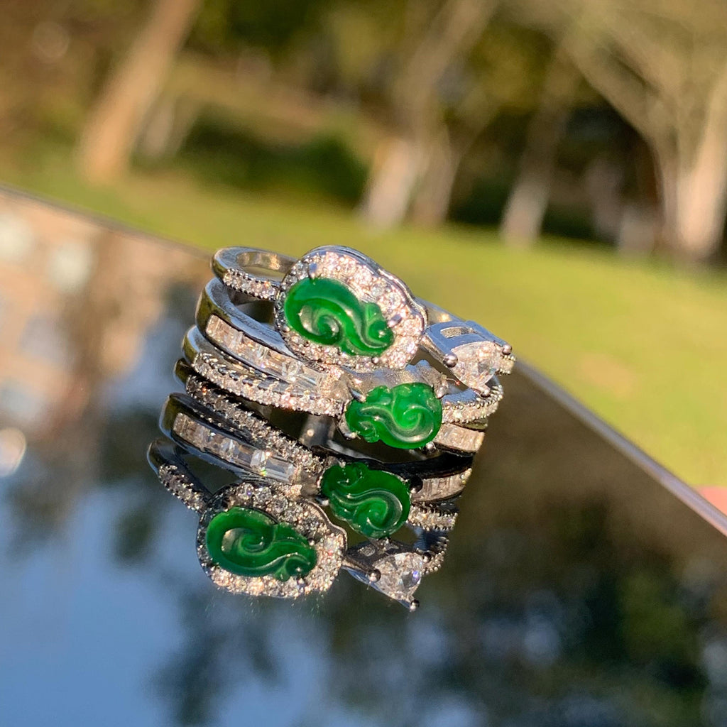 Stack of silver rings with green gemstones on a reflective surface with a blurred natural background