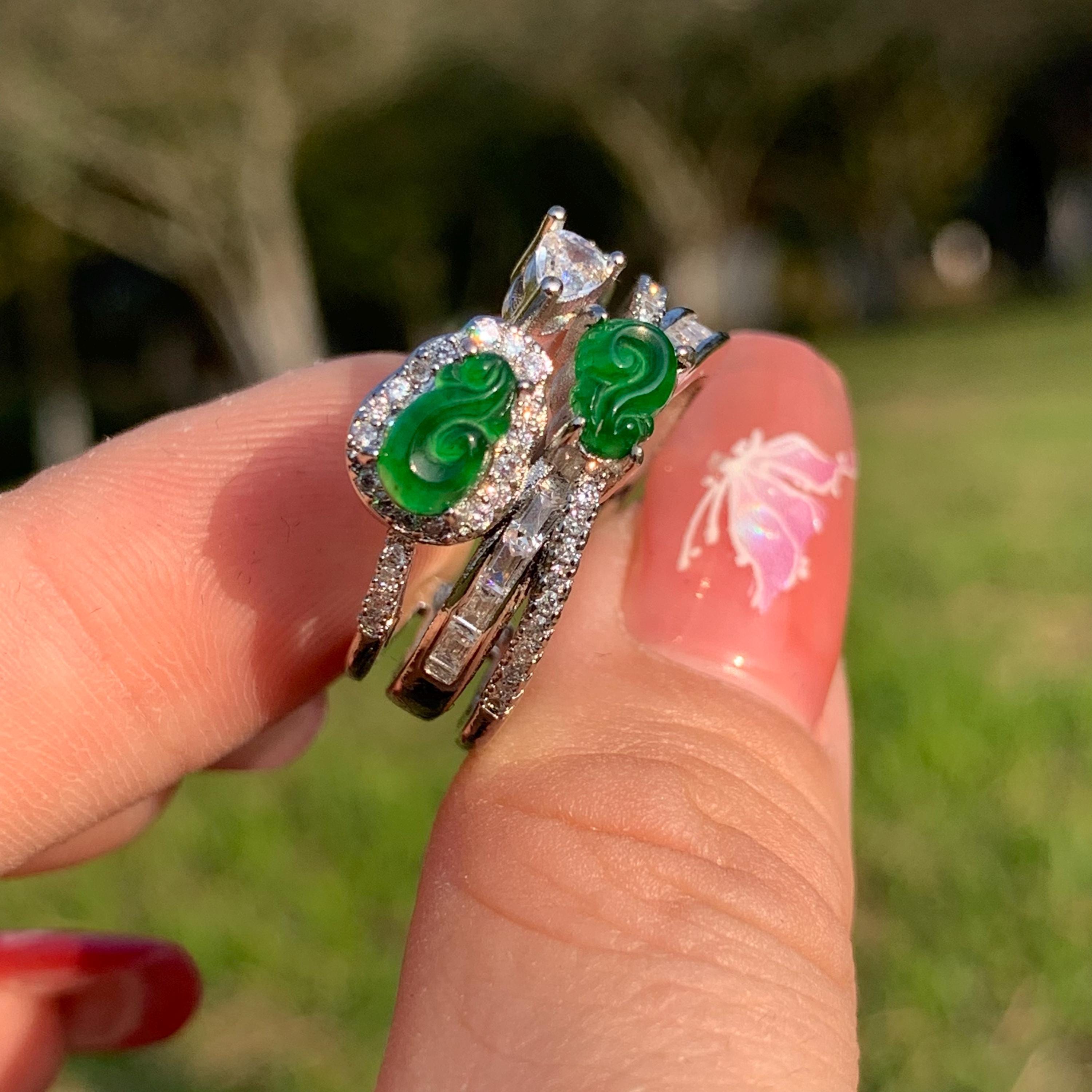 Three rings with green gemstones on a finger against a blurred natural background