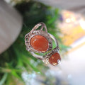 Silver ring with orange gemstones on a blurred green background