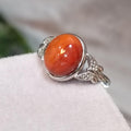 Silver ring with an orange stone on a white surface