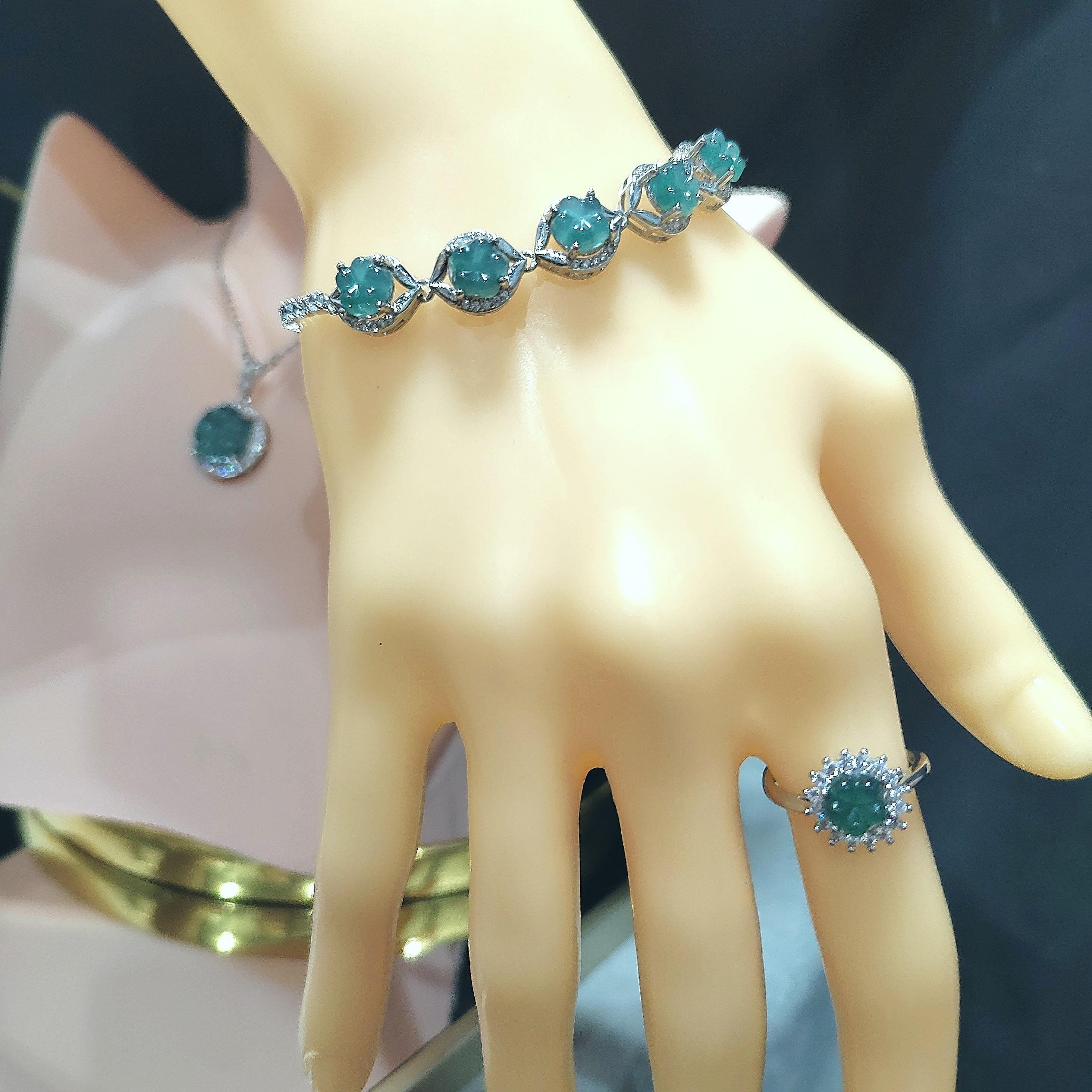 Turquoise gemstone bracelet and ring on a mannequin hand with a dark background