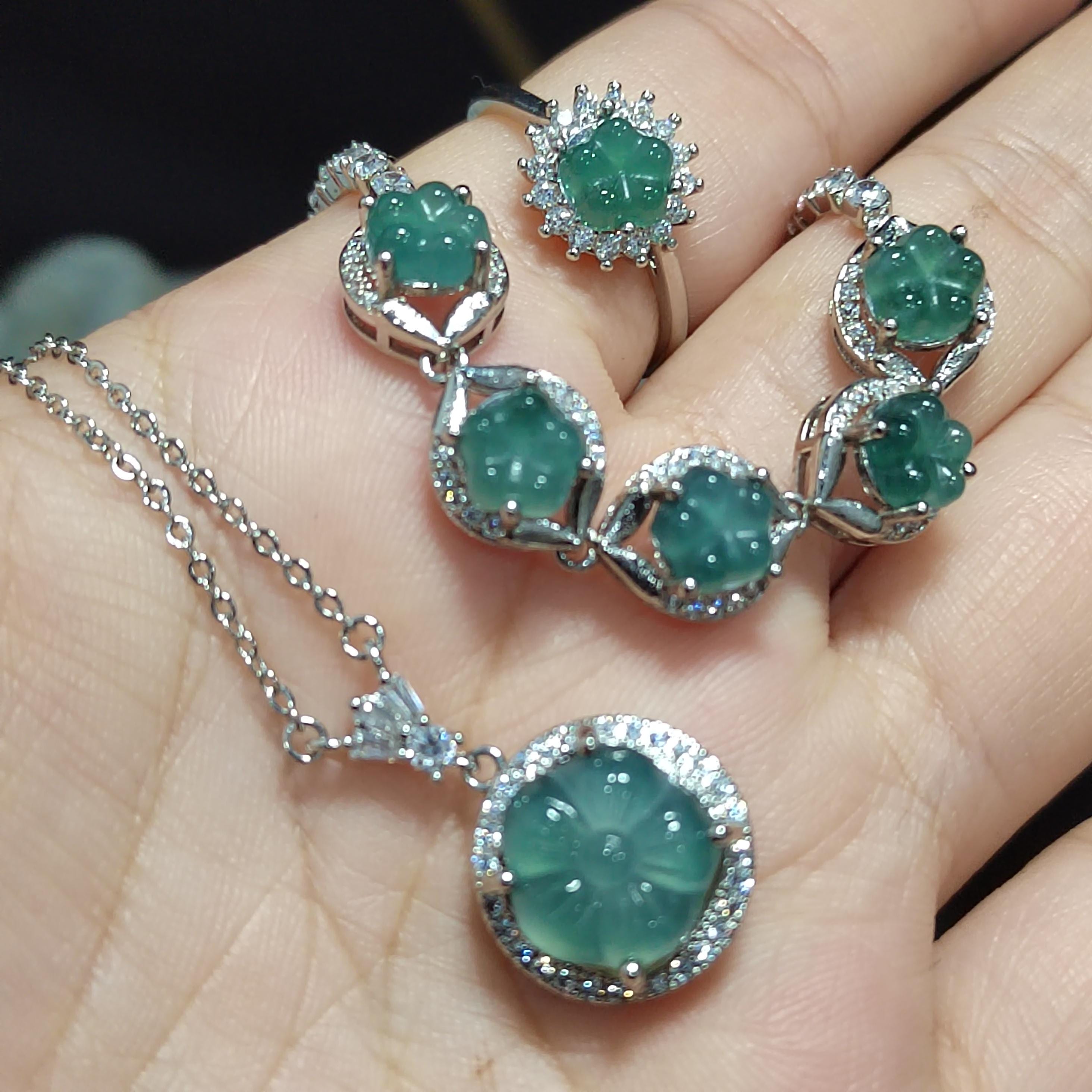 Emerald jewelry set with necklace, earrings, and pendant on a hand.