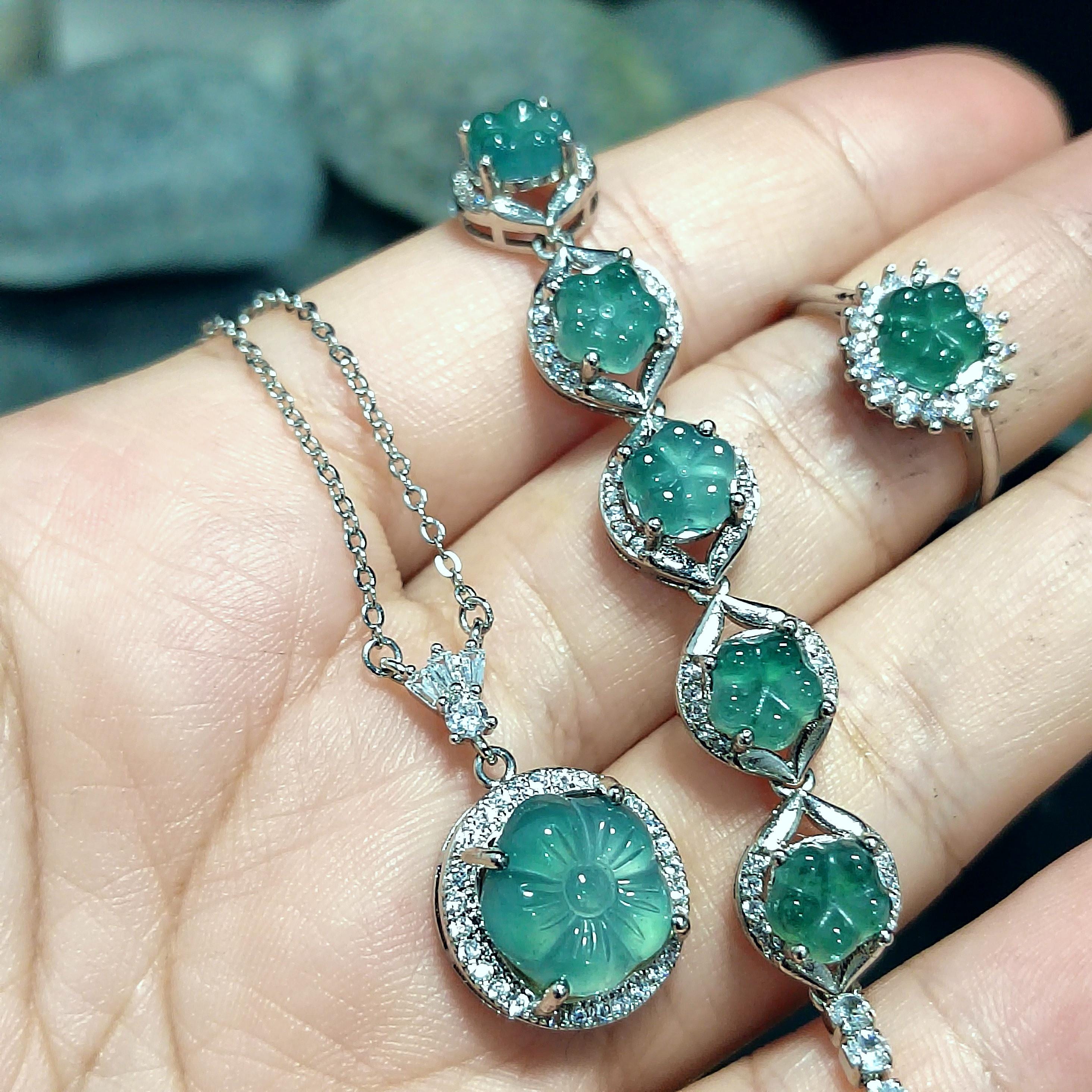 Emerald green gemstone necklace and earrings on a hand with a blurred natural background