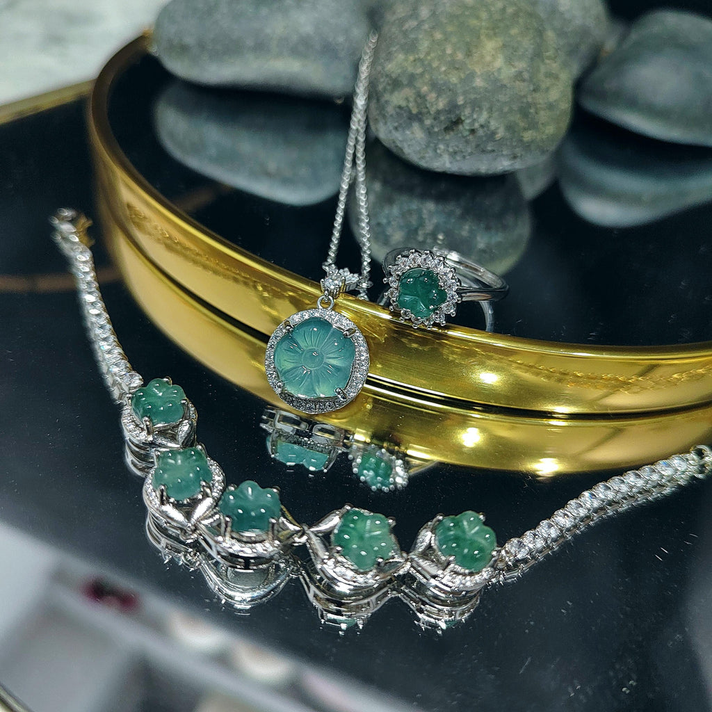 Jewelry set with emerald green stones on a reflective surface