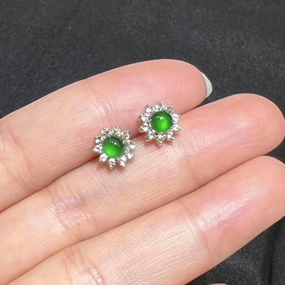 Green gemstone earrings with silver setting held between fingers against a dark background