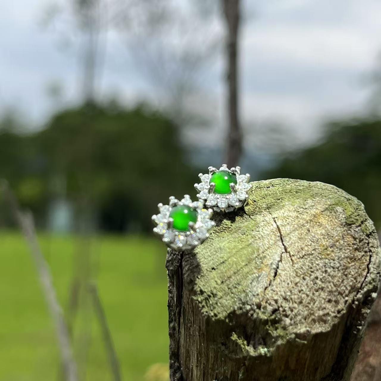 Pair of earrings with green gemstones on a wooden post outdoors