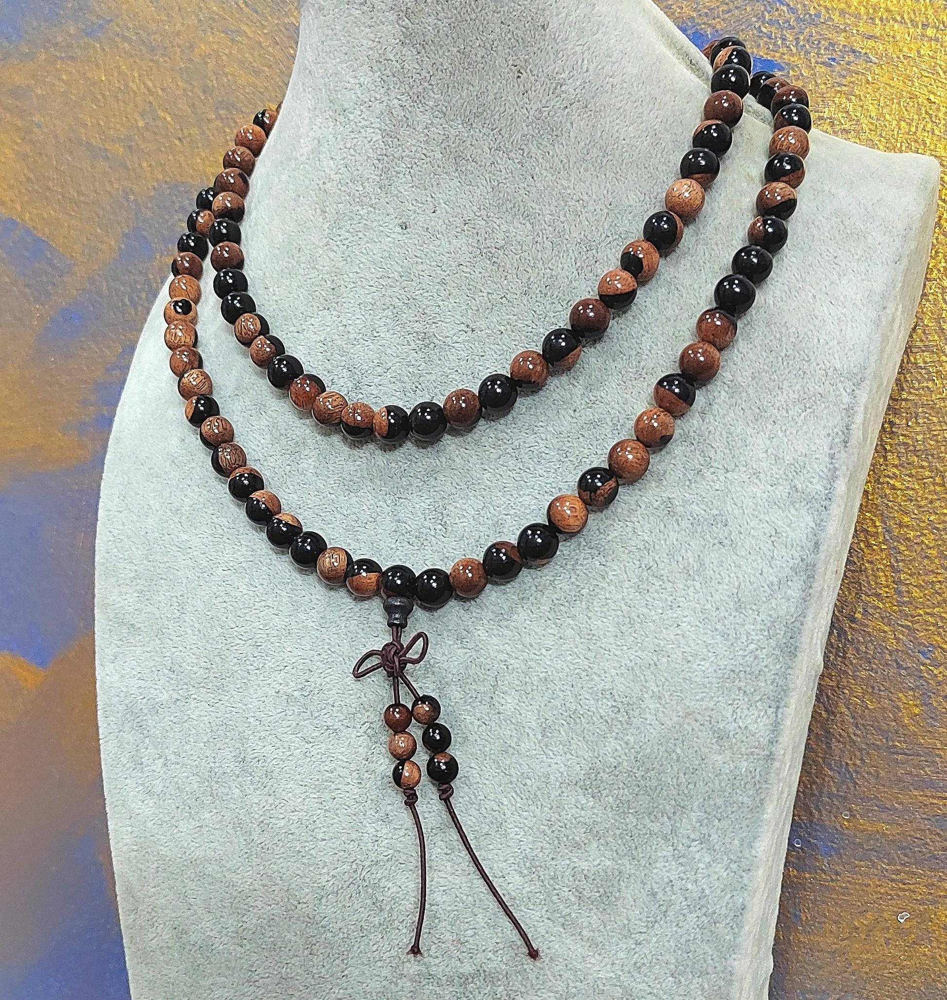 Beaded necklace with a brown cord on a gray stand against a textured surface