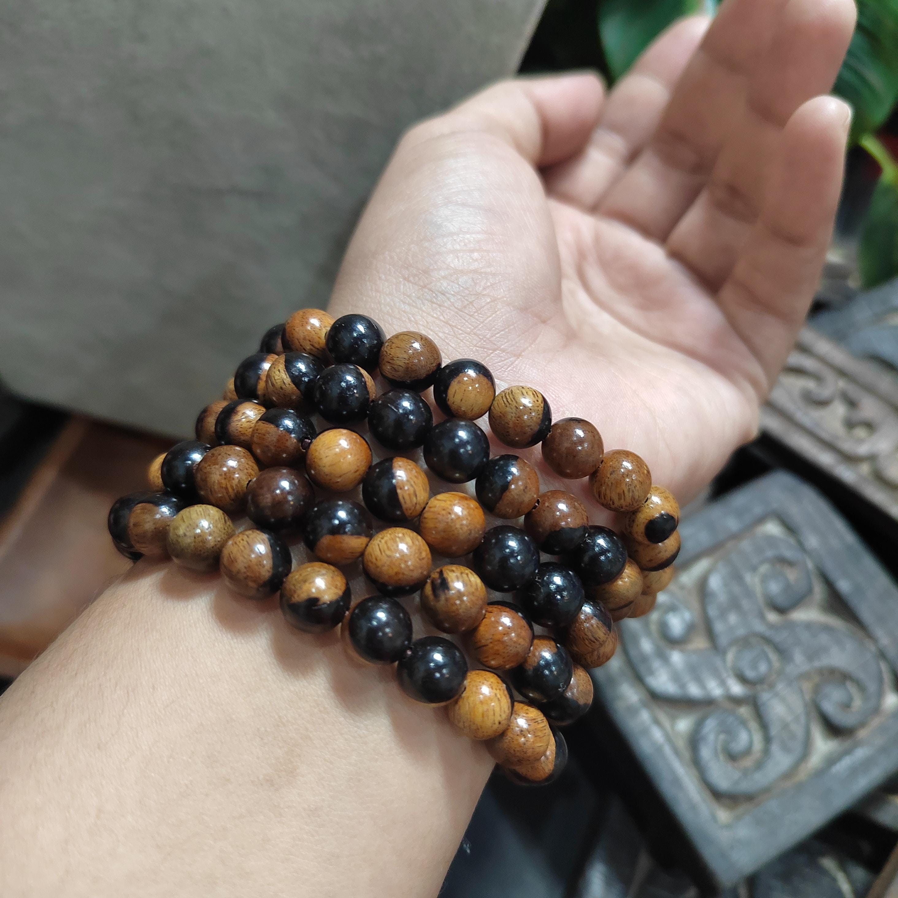 Hand wearing multiple black and brown beaded bracelets with a blurred background